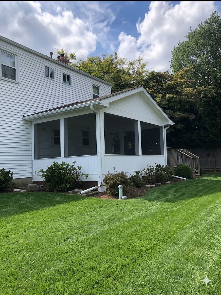 White house with screened porch and green lawn under a partly cloudy sky