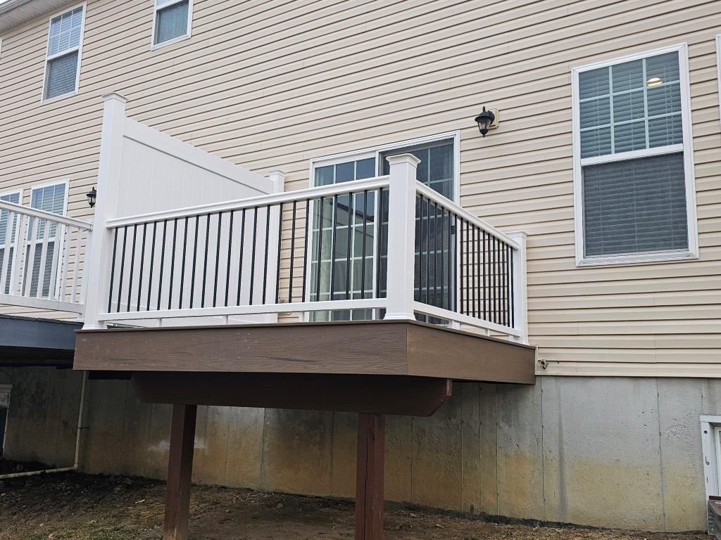 A deck with a white railing is in front of a house.