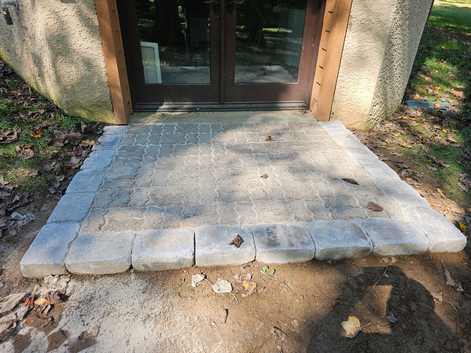 Stone patio entrance to a building with double doors. Gray pavers and border.