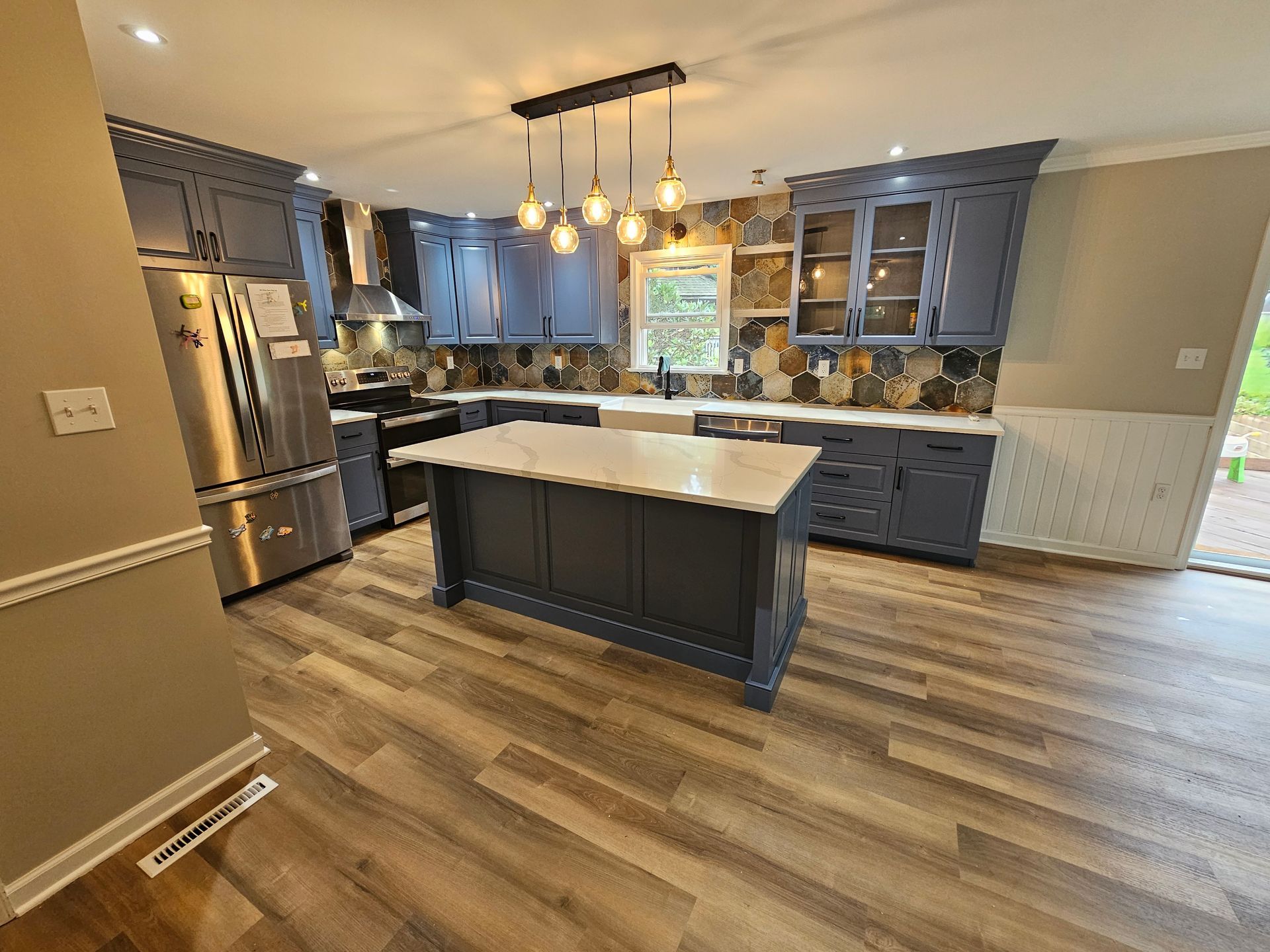 Modern kitchen with gray cabinets, island, stainless steel appliances, and hexagon tile backsplash.