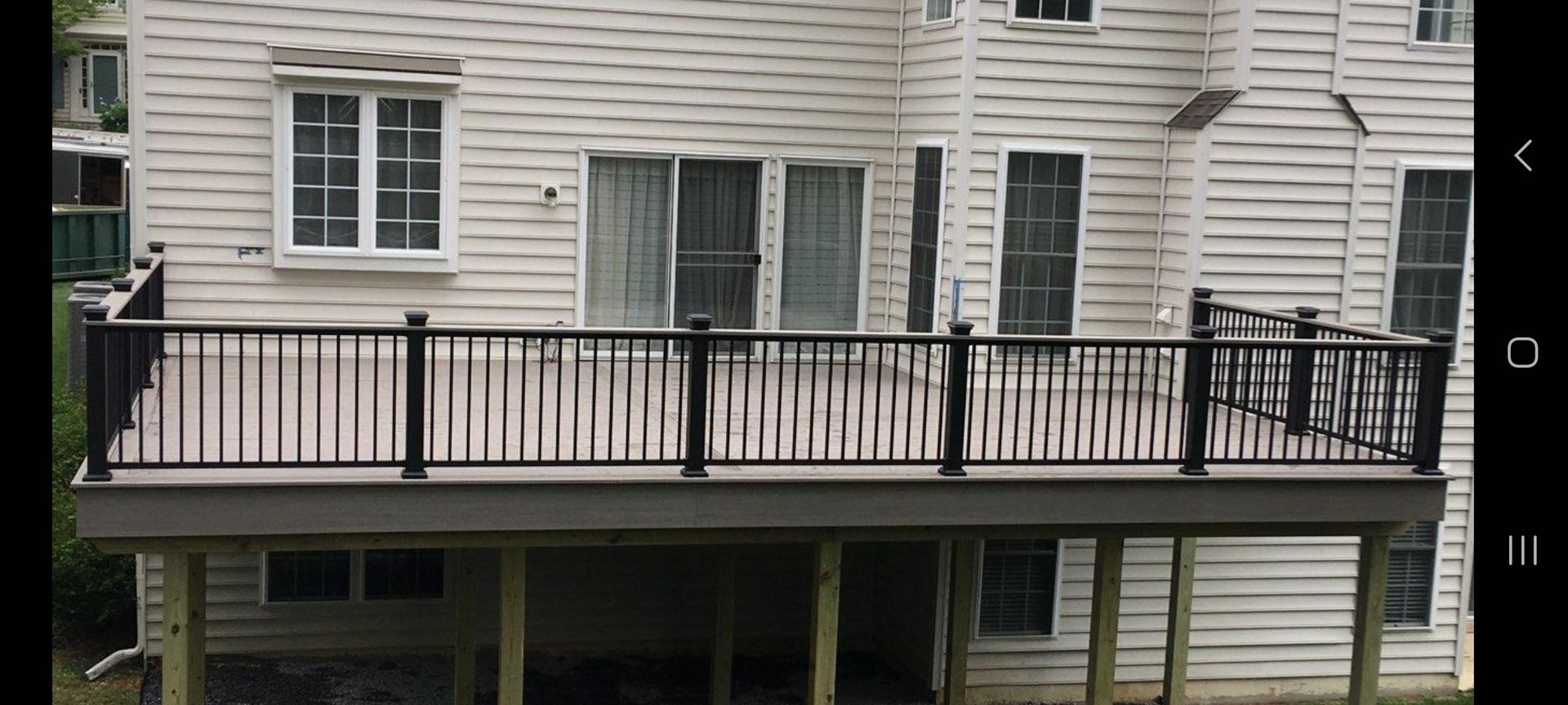A large deck with a black railing is in front of a white house