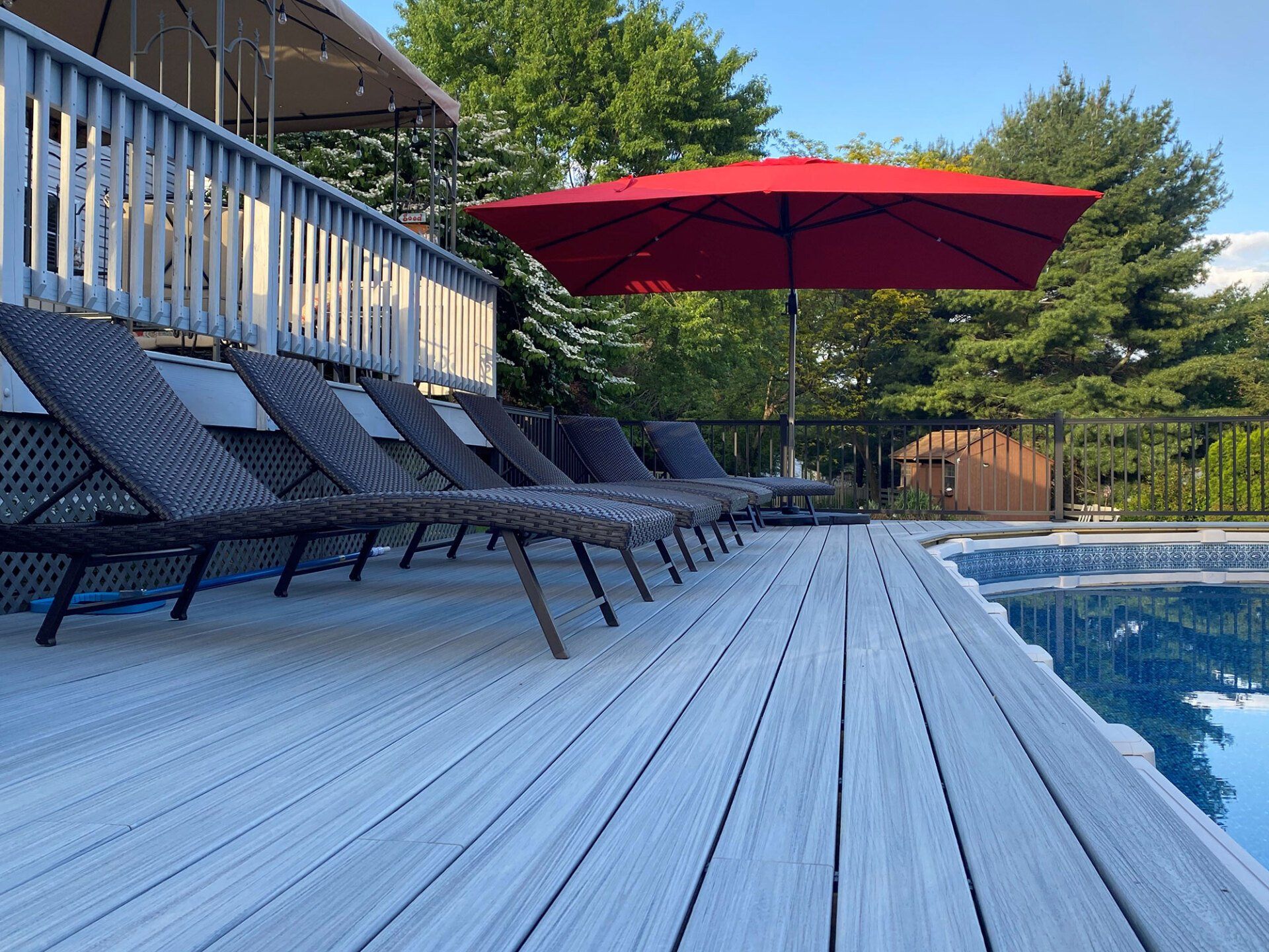A deck with chairs and an umbrella next to a swimming pool