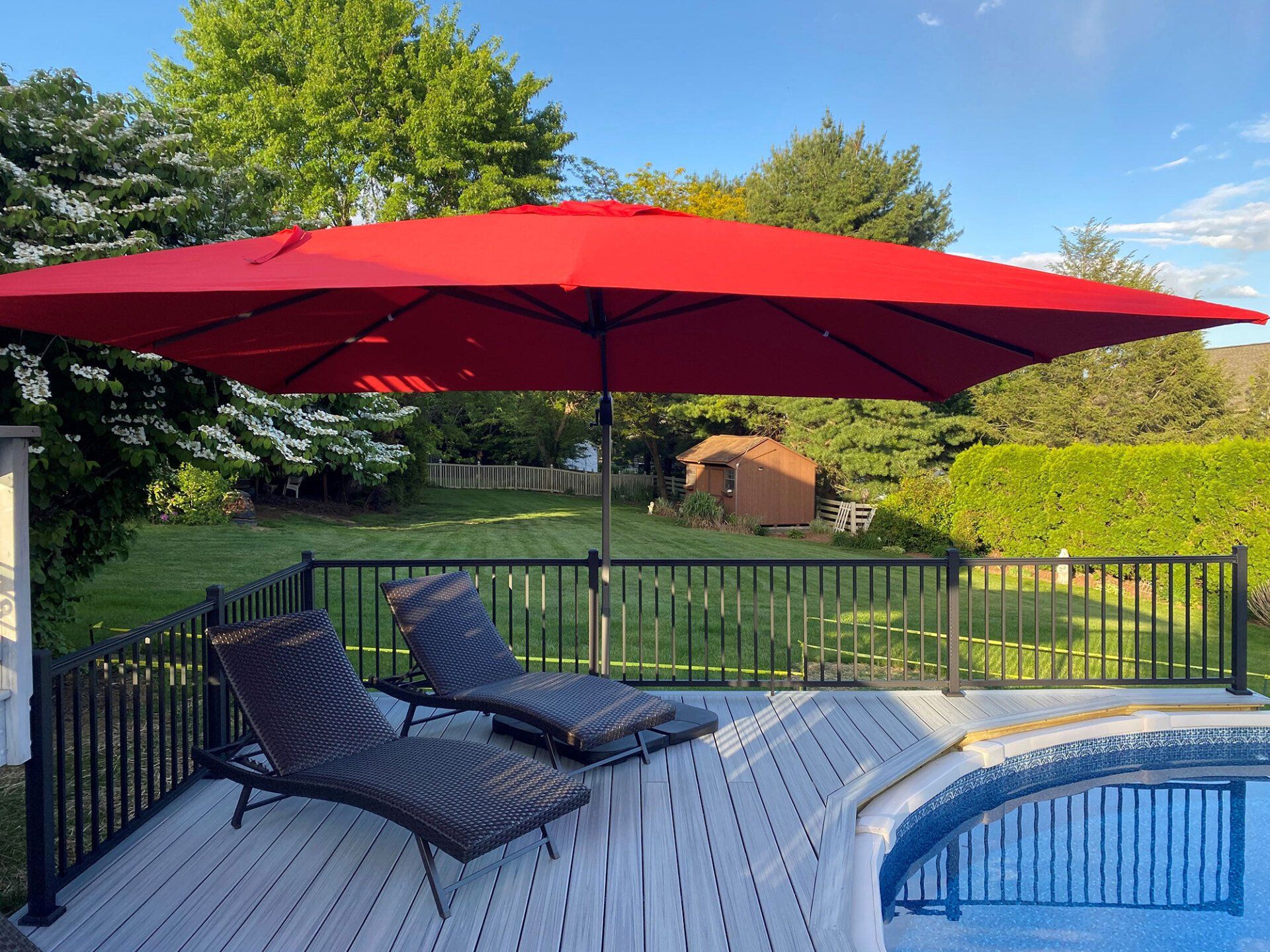 A large red umbrella is sitting on a deck next to a pool