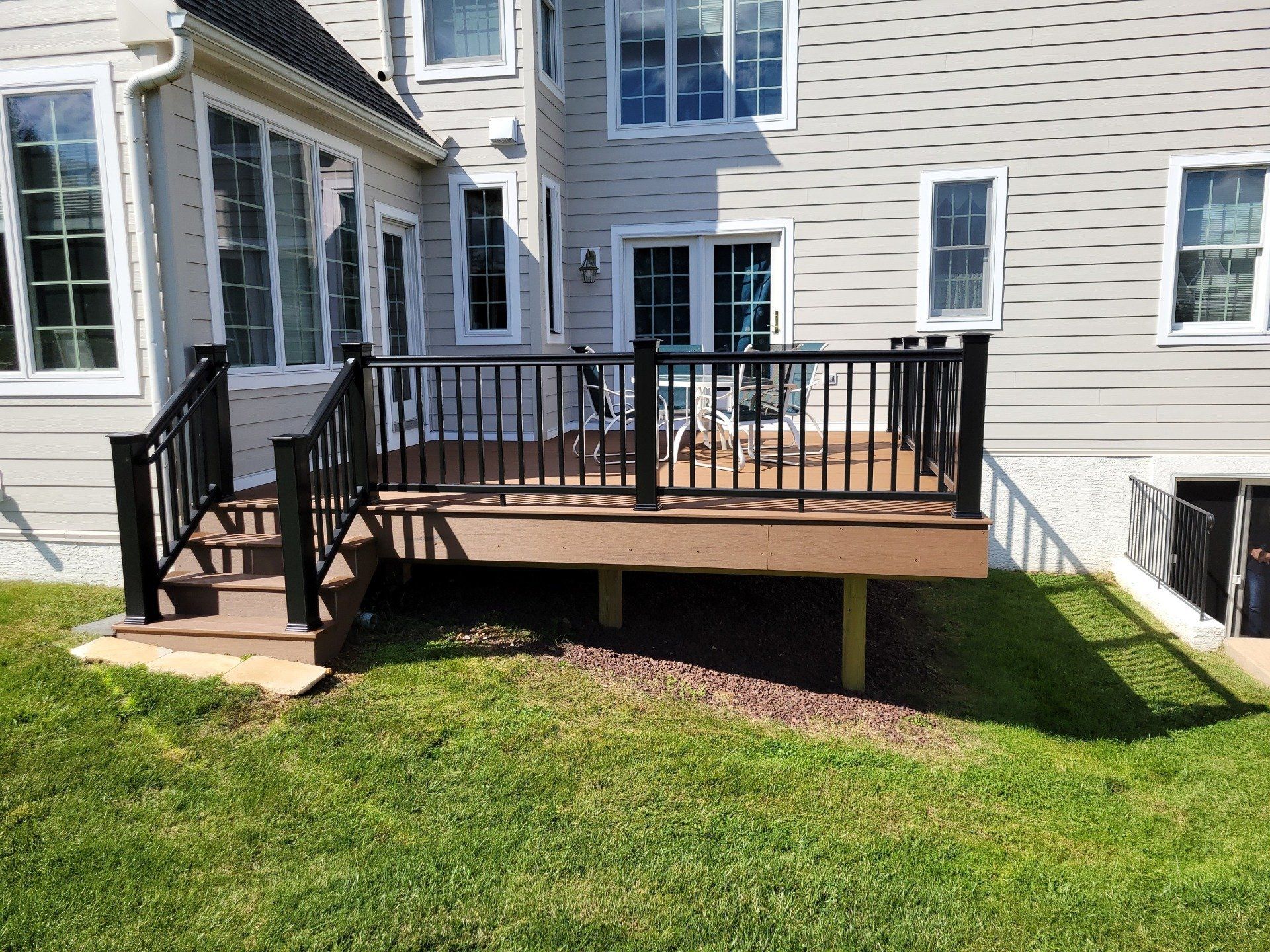 A large deck with a black railing is in the backyard of a house