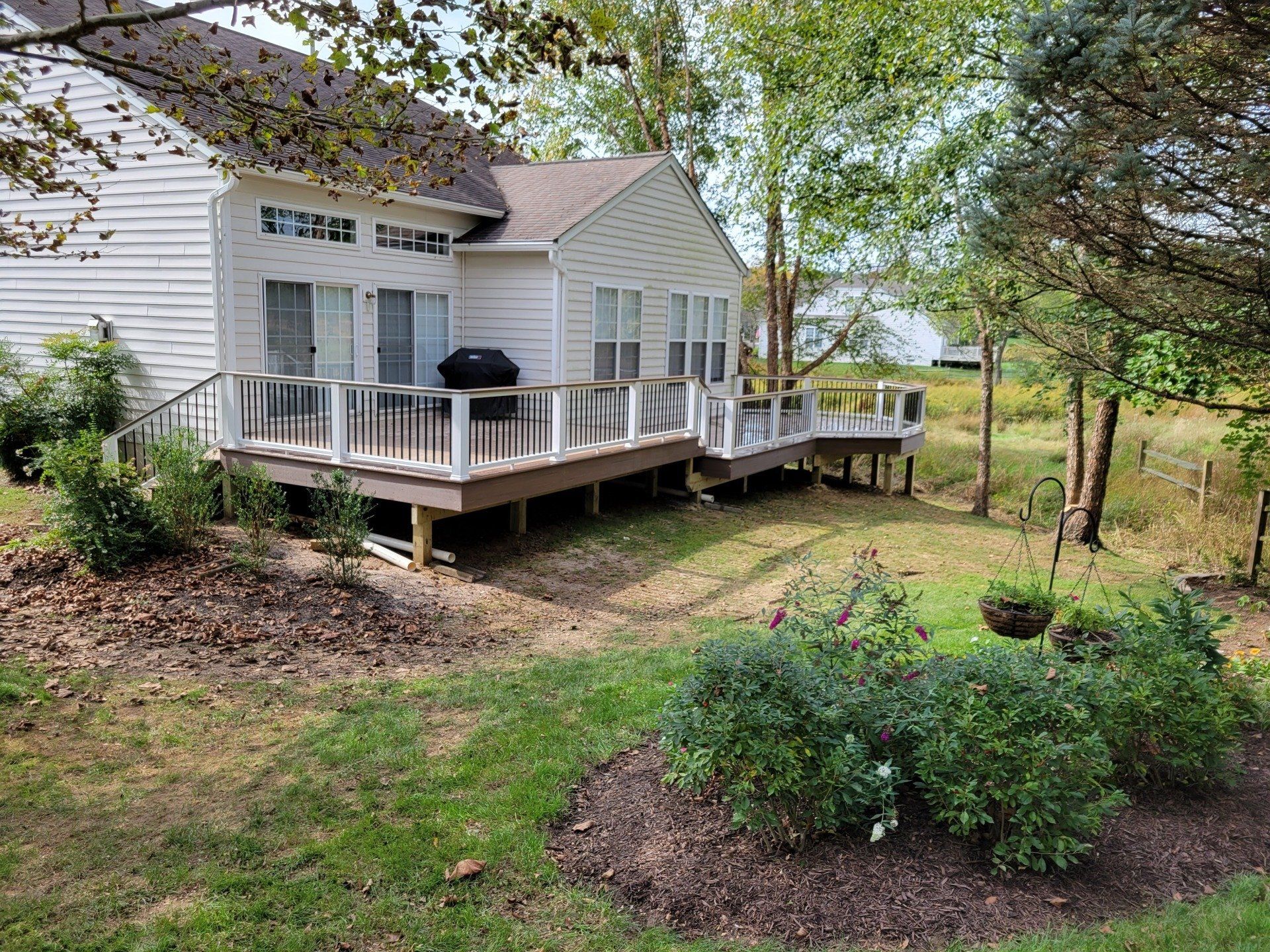 A white house with a large deck and a grill in the backyard