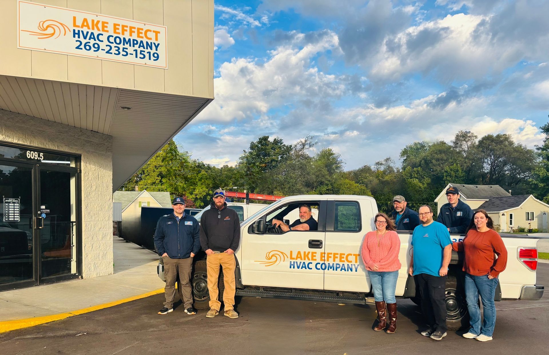 Lake Effect HVAC team posing by their truck in front of their office. Sunny day.