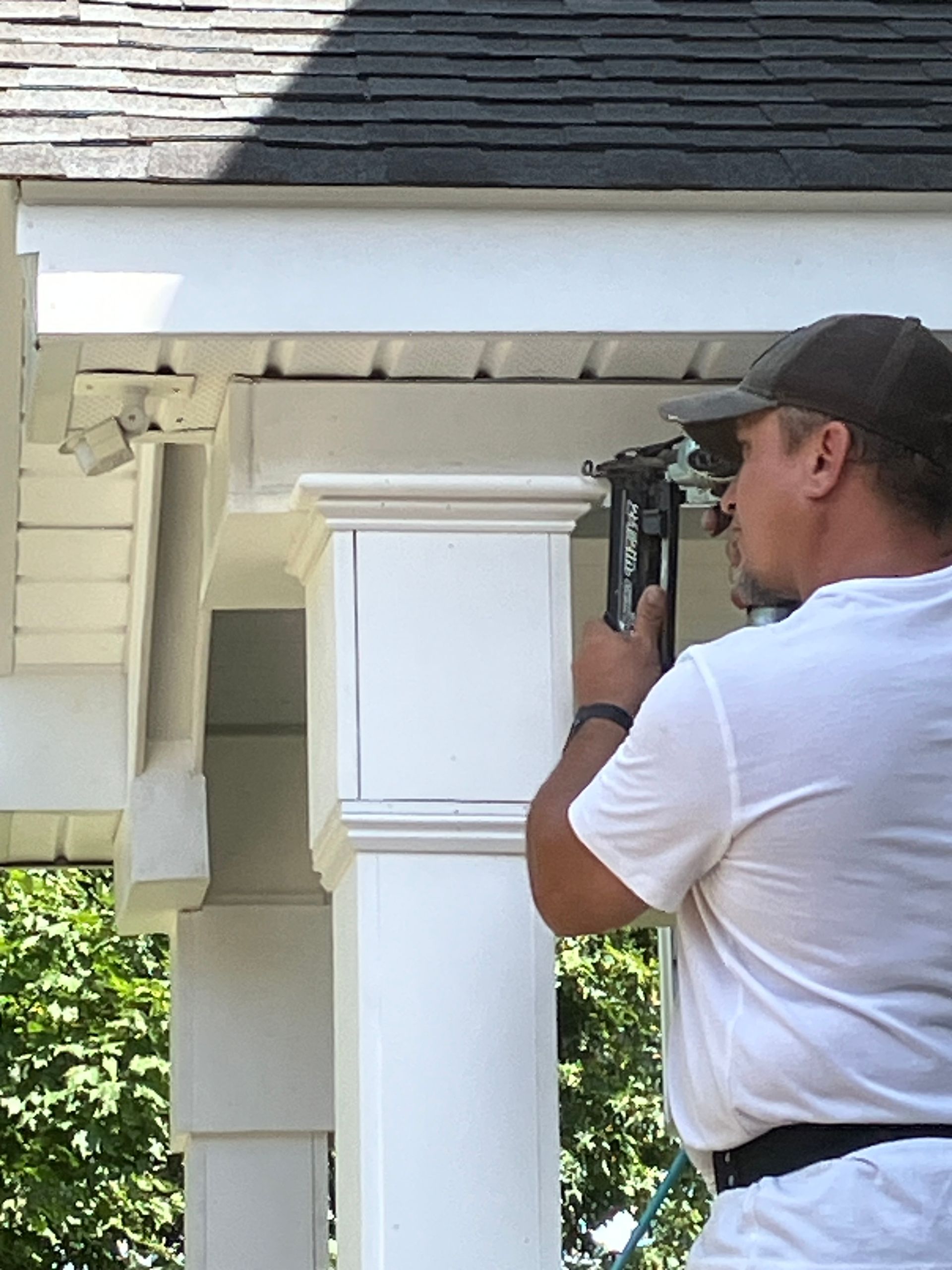 A man is standing on the porch of a house nailing a house stand.