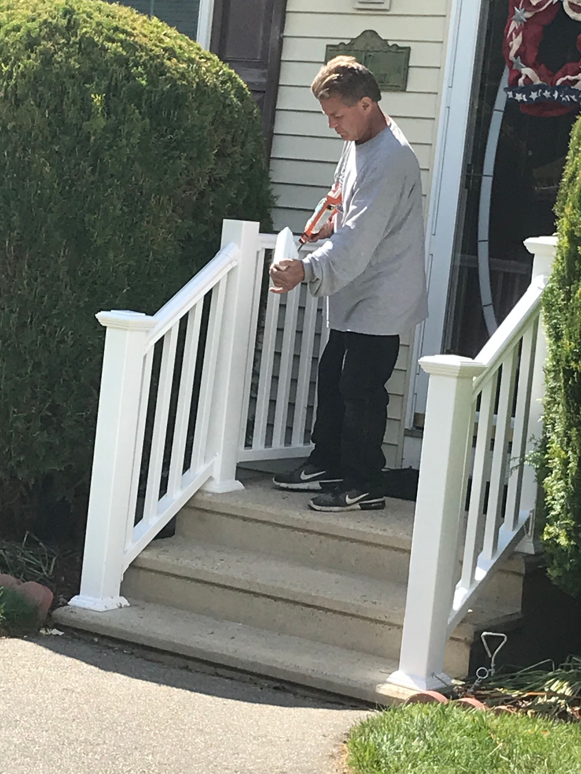A man is standing on the porch of a house holding a cup of coffee.
