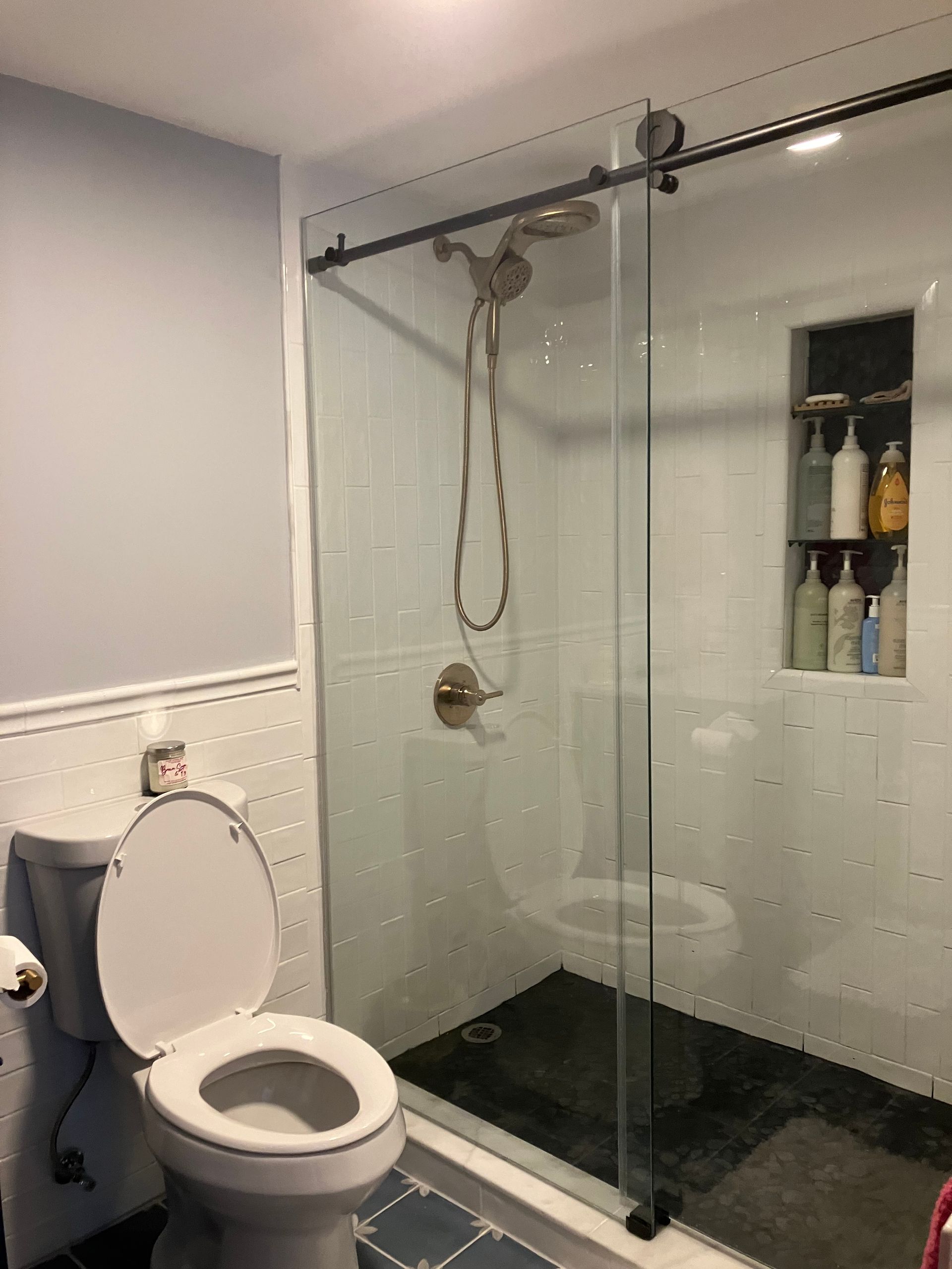 A bathroom with a toilet , shower and sliding glass door.