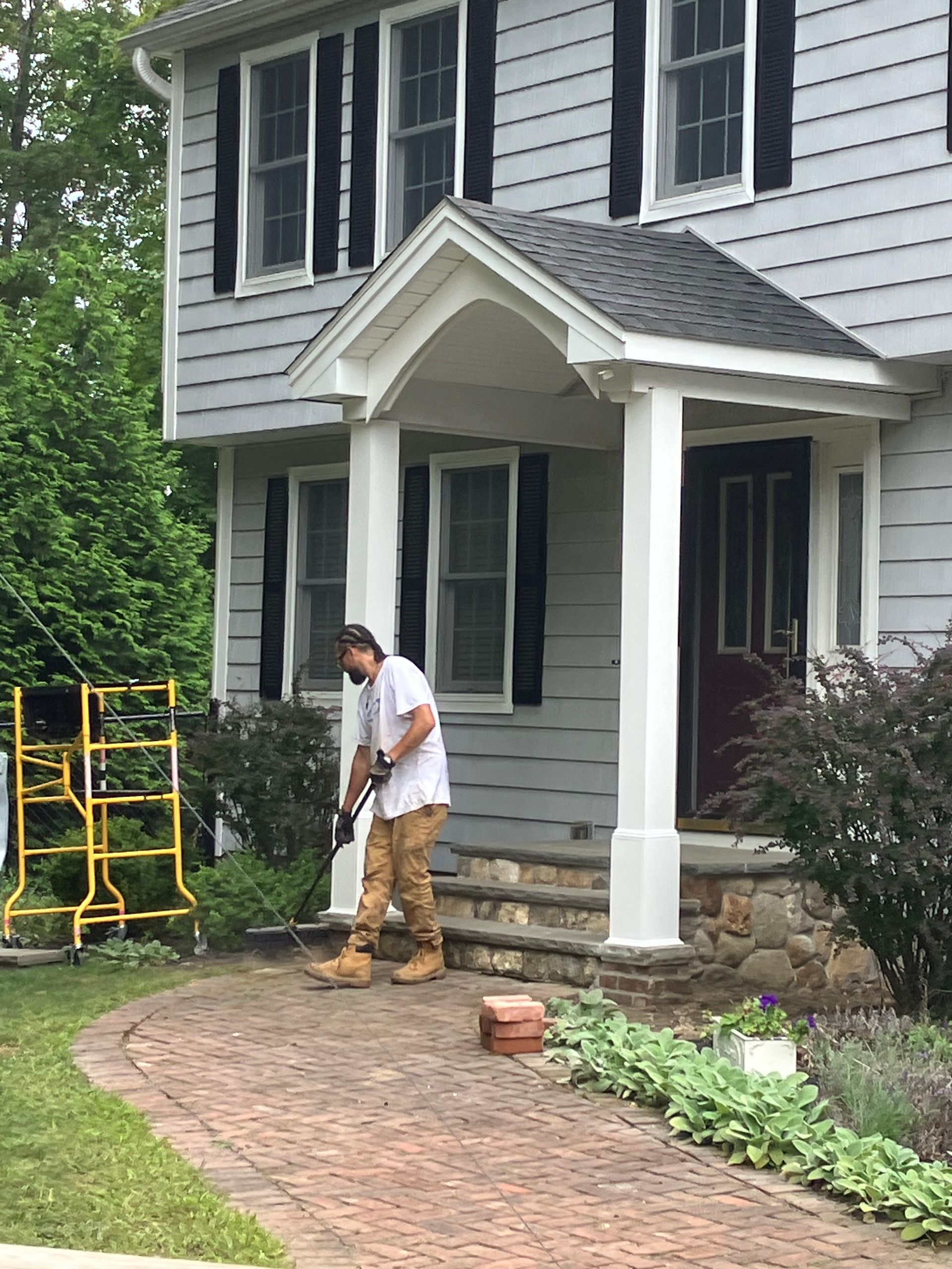 A man is standing in front of a house holding a shovel.