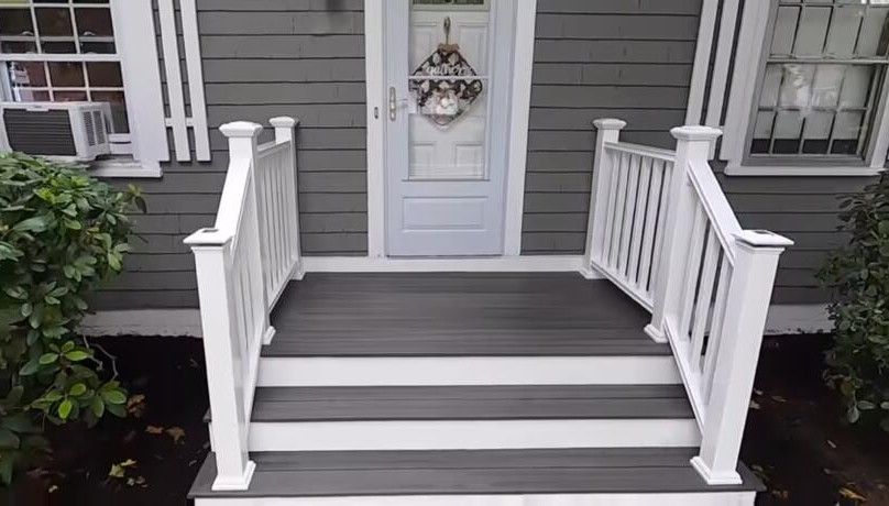 A gray house with a white porch and stairs leading to the front door.