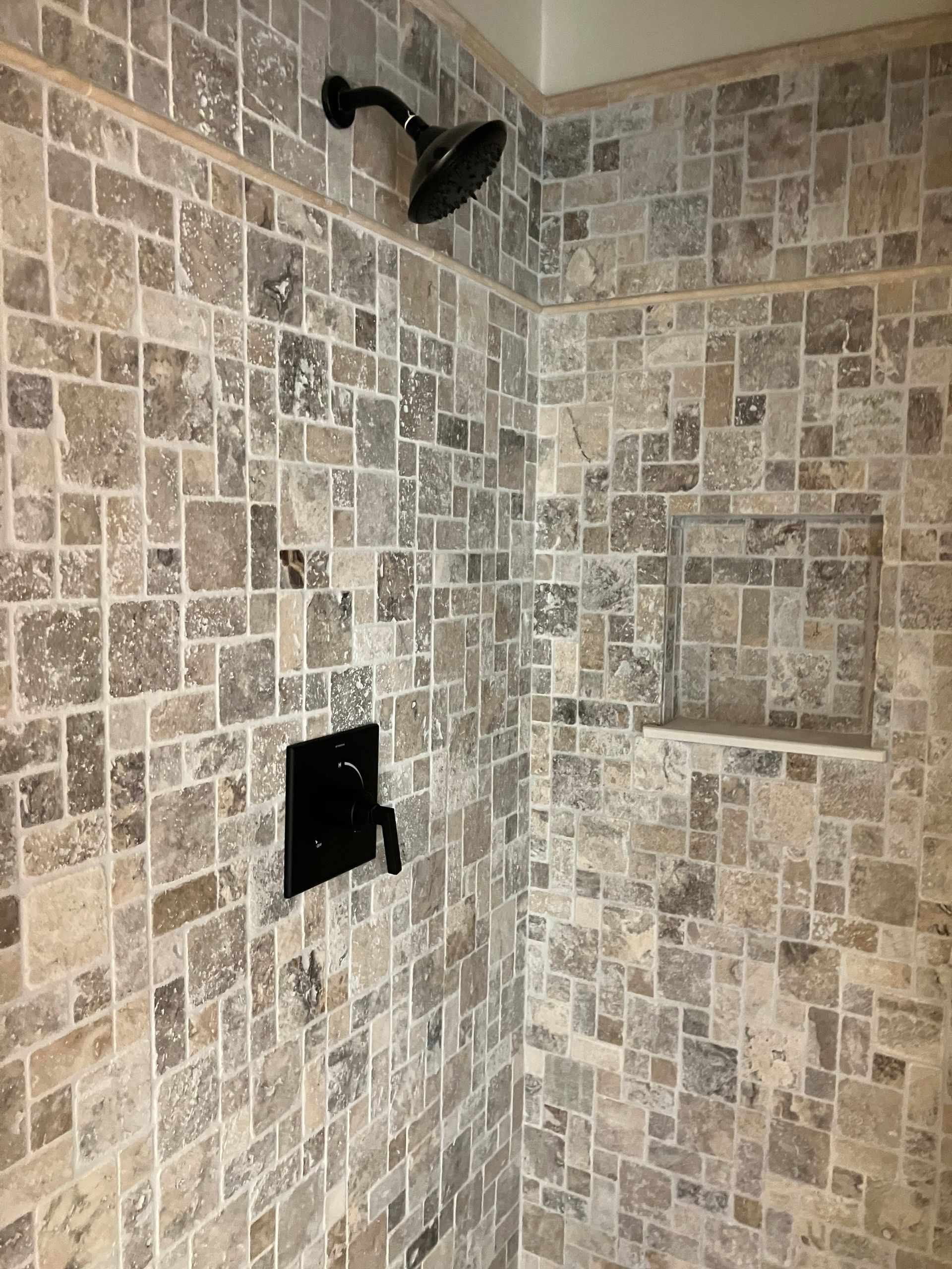 A shower with a tiled wall and a shower head.