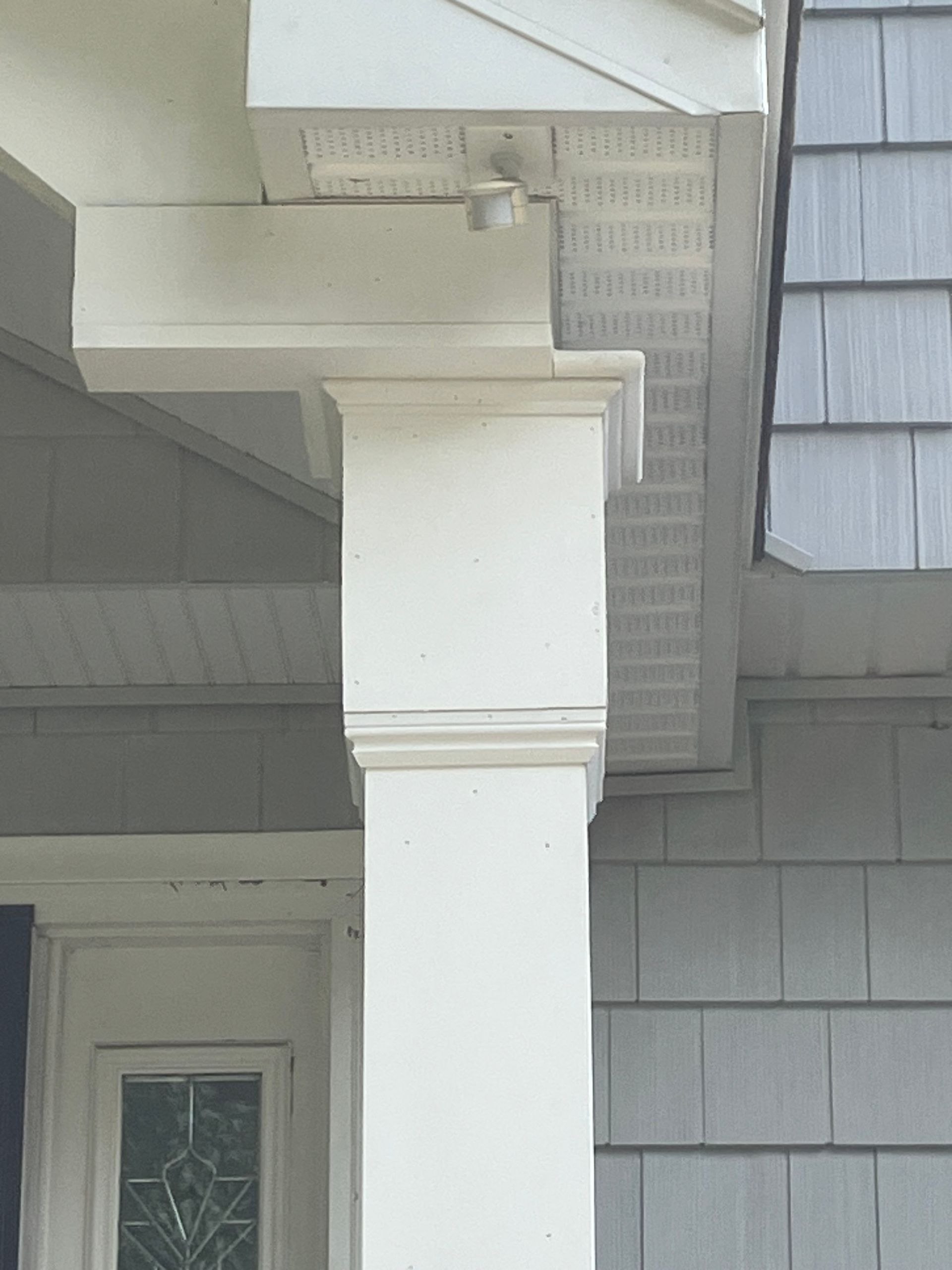 A white pillar on the side of a house with a window.