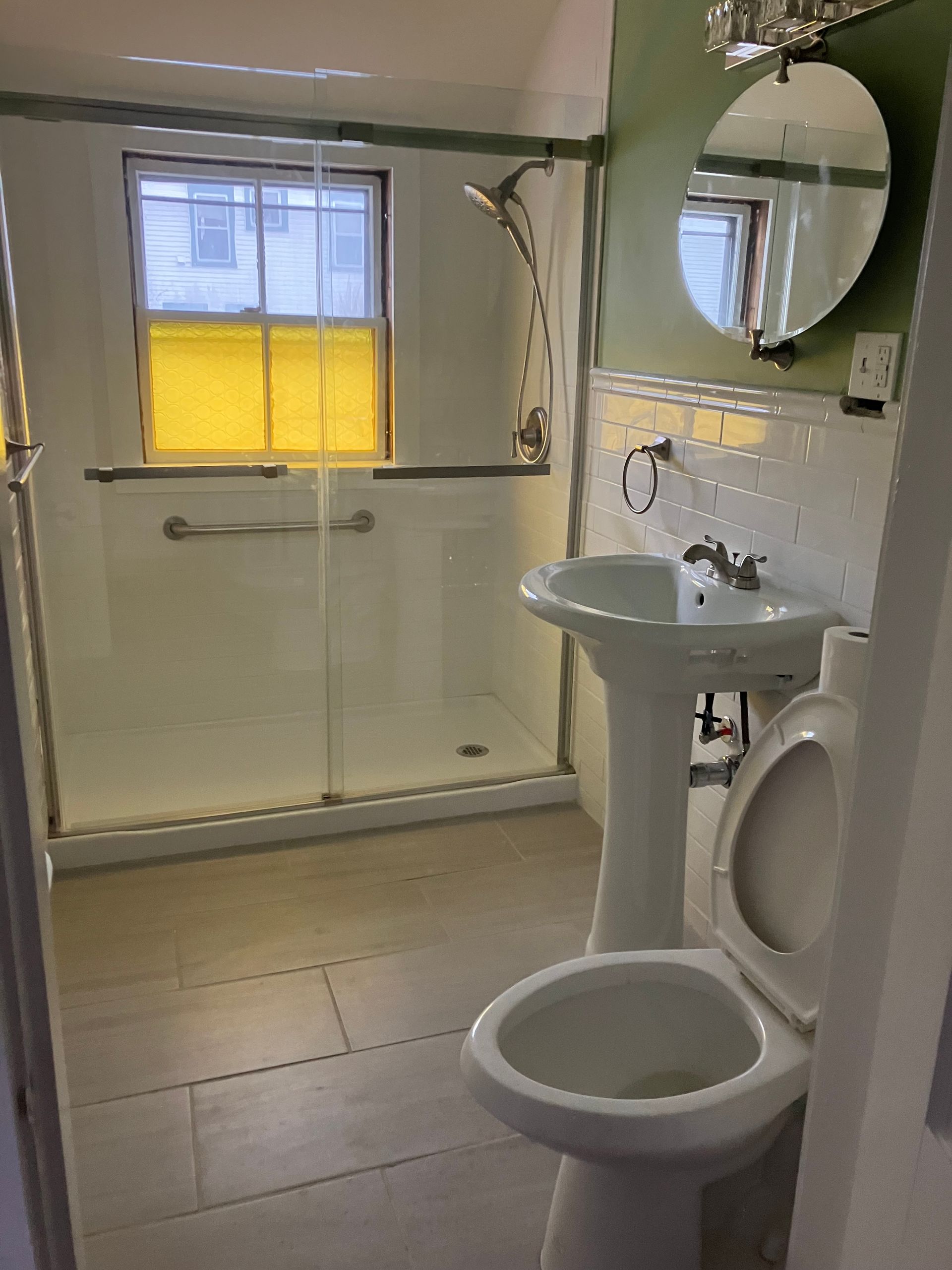A bathroom with a toilet , sink , shower and mirror.