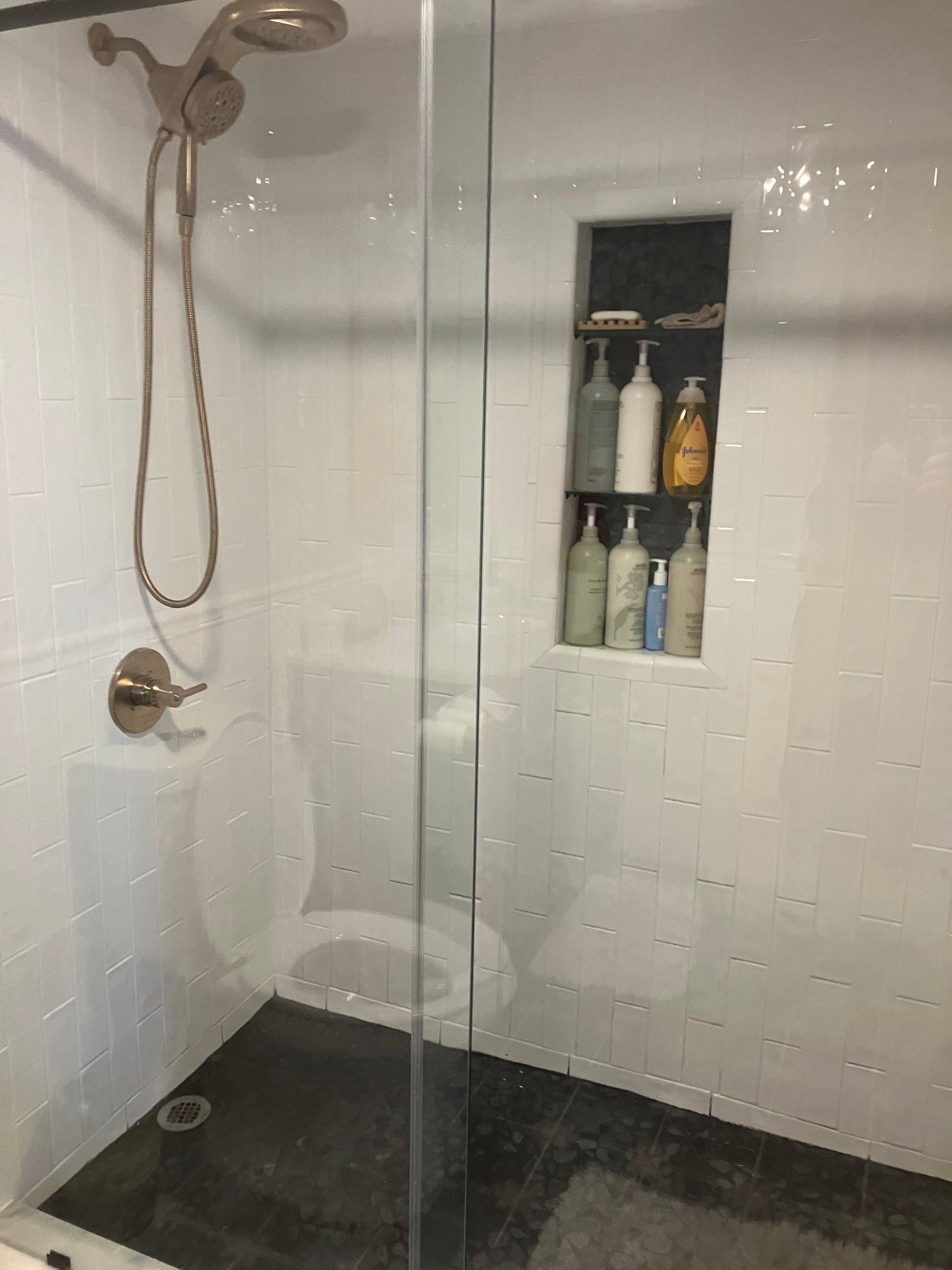 A bathroom with a walk in shower , toilet , and soap shelf.