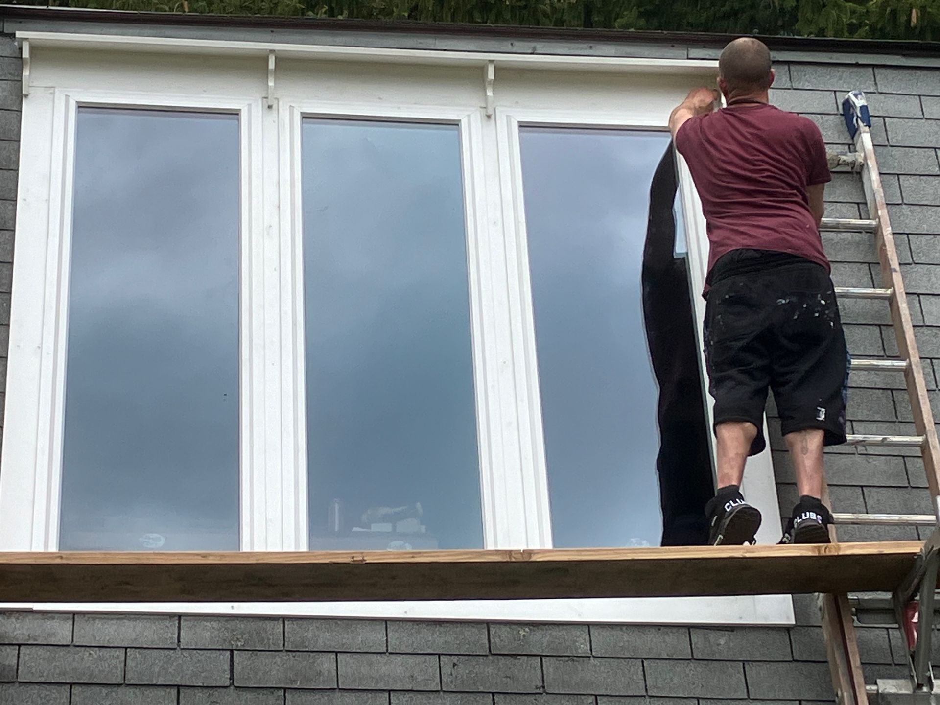 A man is standing on a ladder in front of a window.