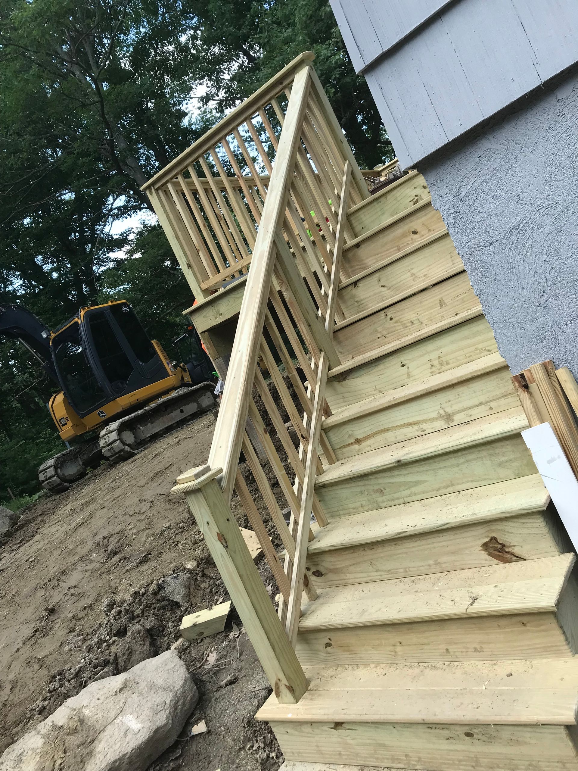 A wooden deck with stairs and a bulldozer in the background.
