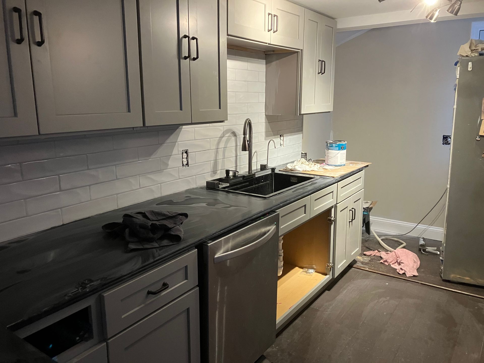 A kitchen with gray cabinets , a sink , a stove , and a dishwasher.