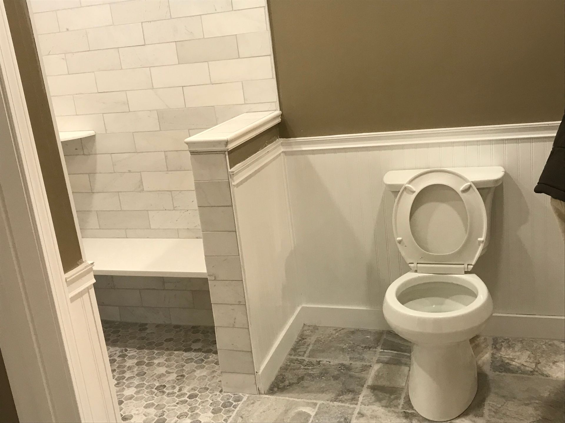 A bathroom with a toilet , shower , and bench.