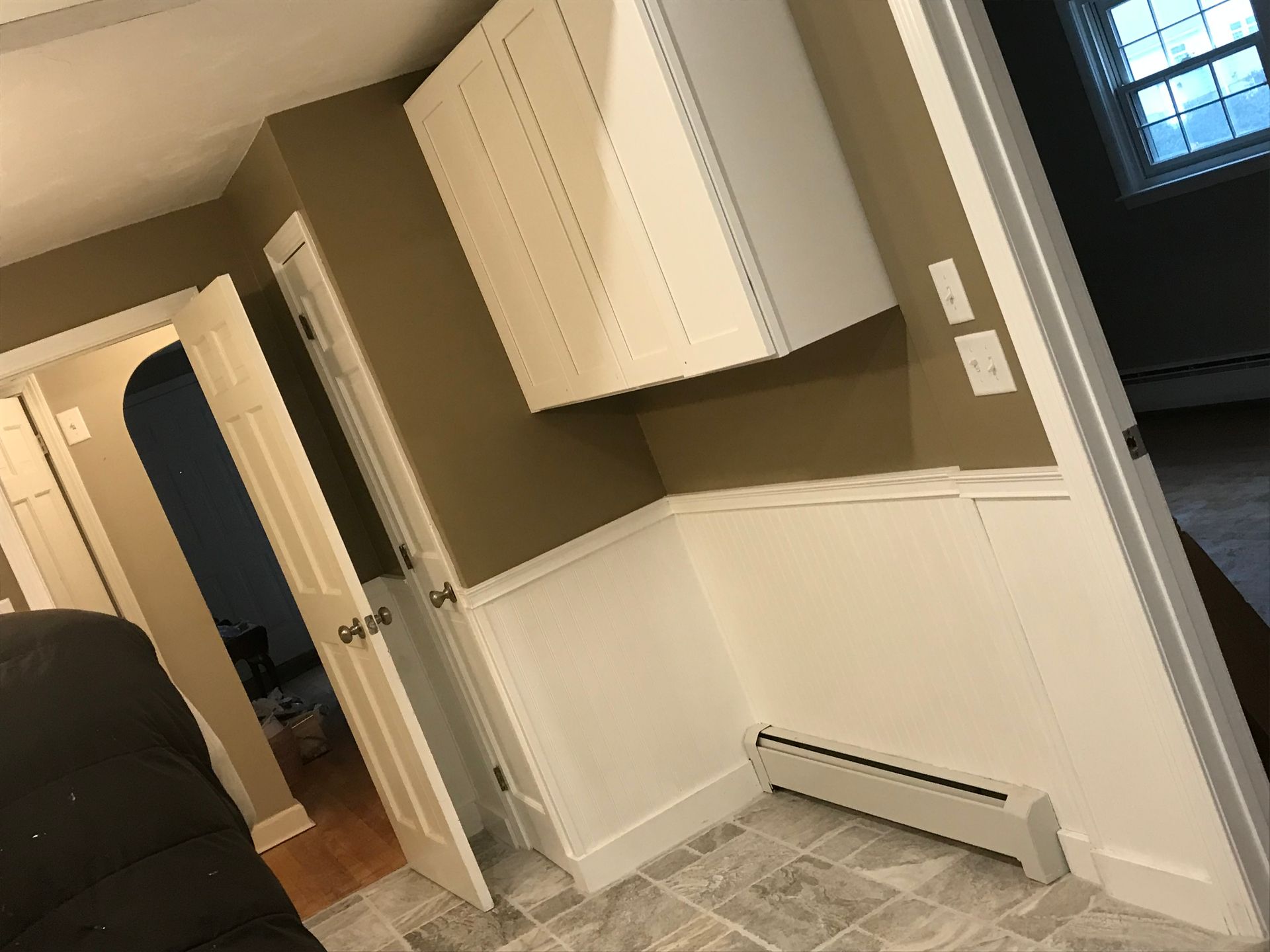 A room with a couch , cabinets , and a radiator on the floor.