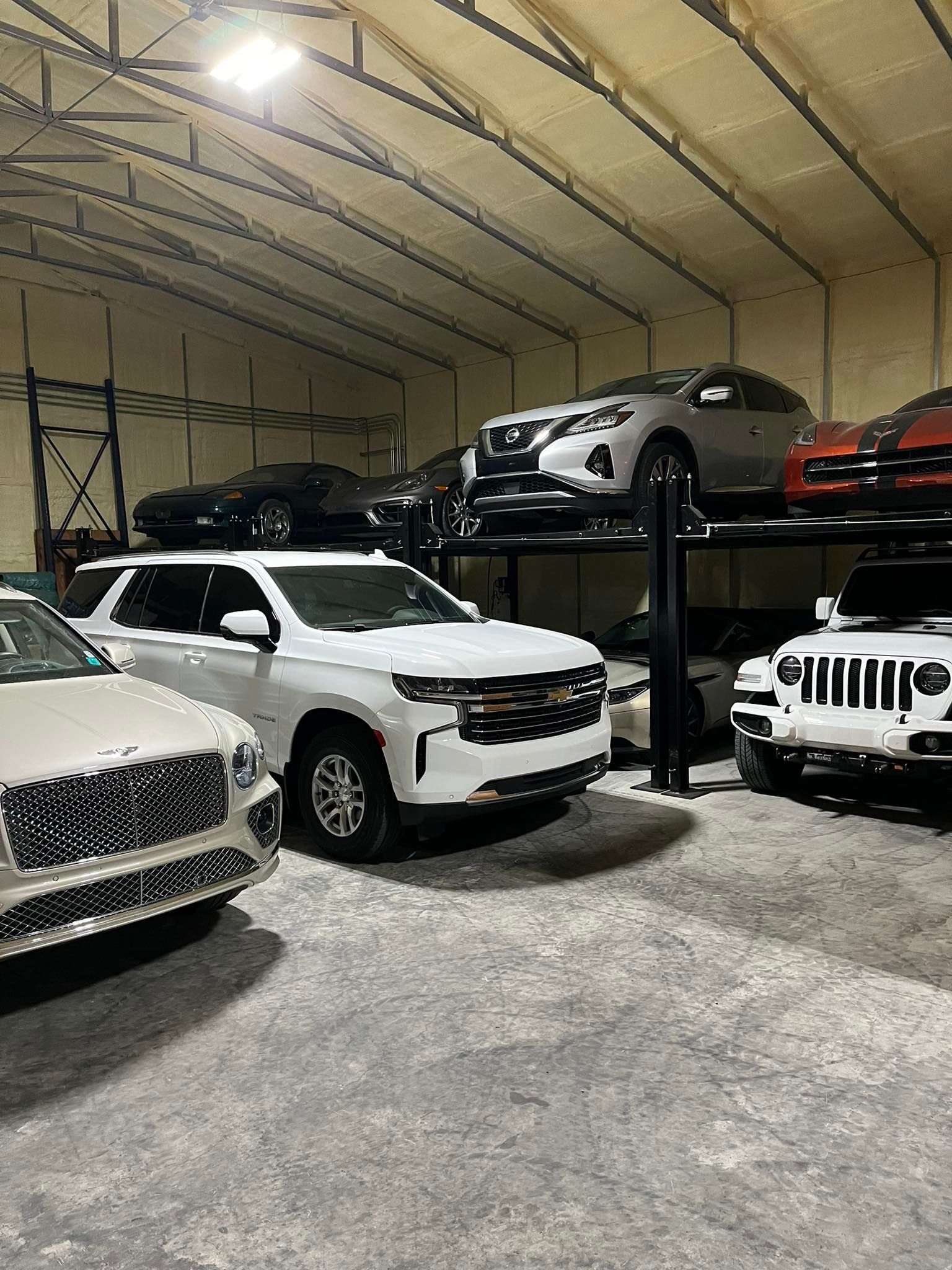 An indoor garage with several cars, including a white SUV and a silver car on a lift.