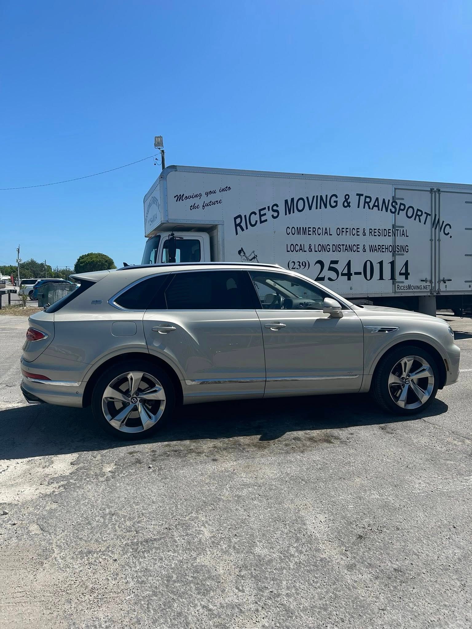 A silver luxury SUV parked on a gravel lot next to a white box truck with 