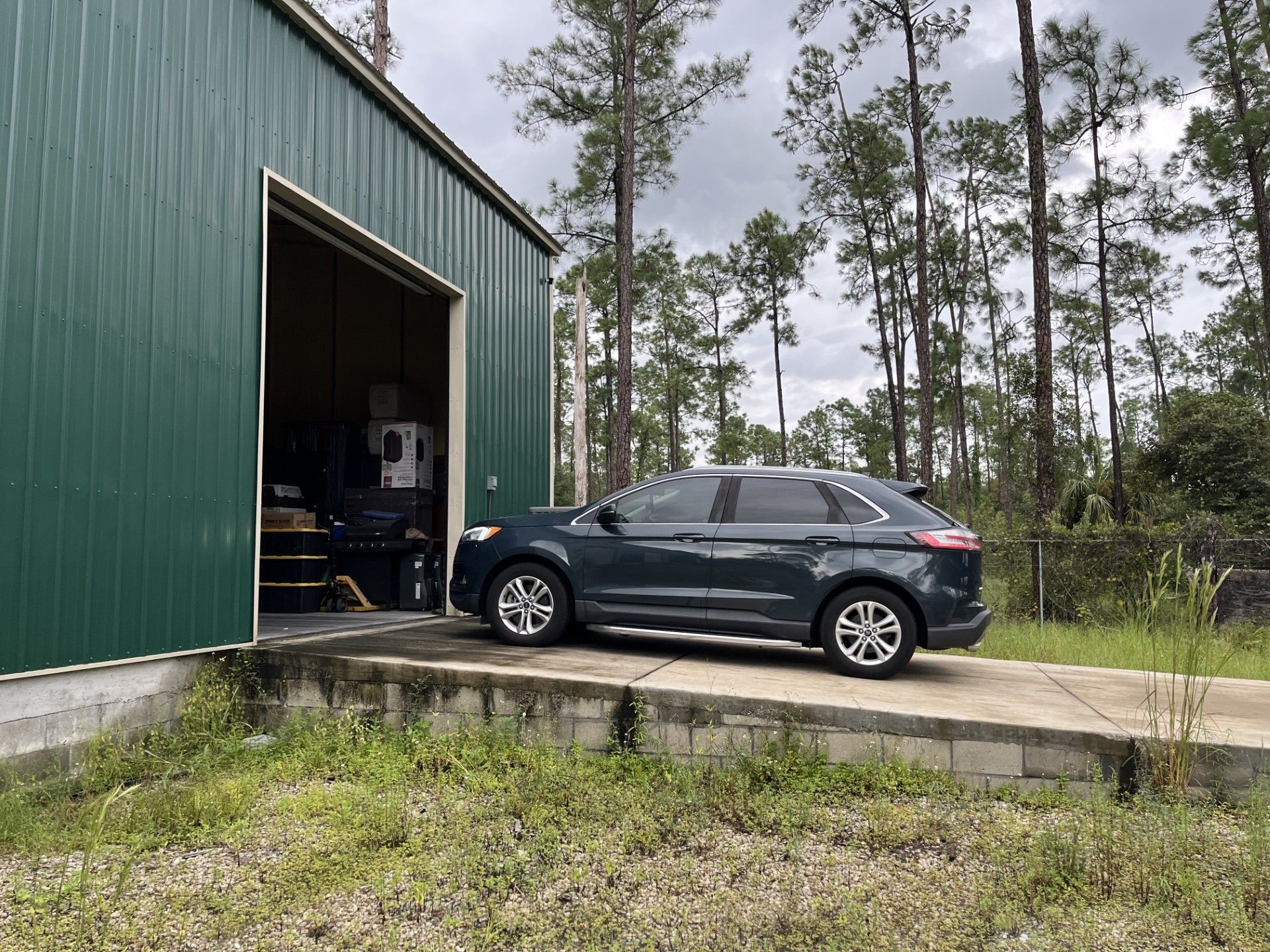 A dark gray SUV parked on a concrete ramp leading into the open doorway of a green metal storage building.