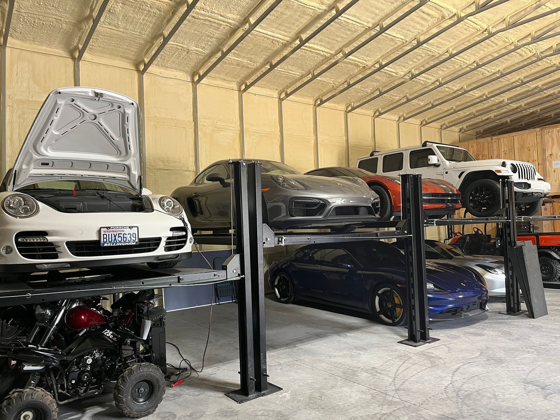 A spacious garage featuring multiple cars parked on stacked lifts, including a white Porsche and a blue sports car.