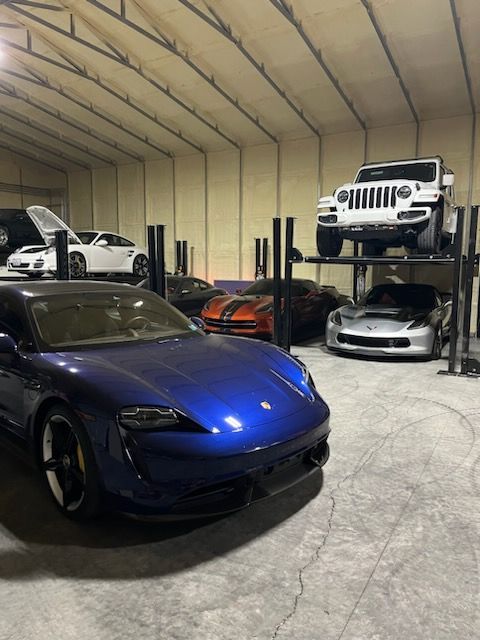 A garage interior featuring a blue sports car in the foreground and several other vehicles, including a Jeep, on lifts.