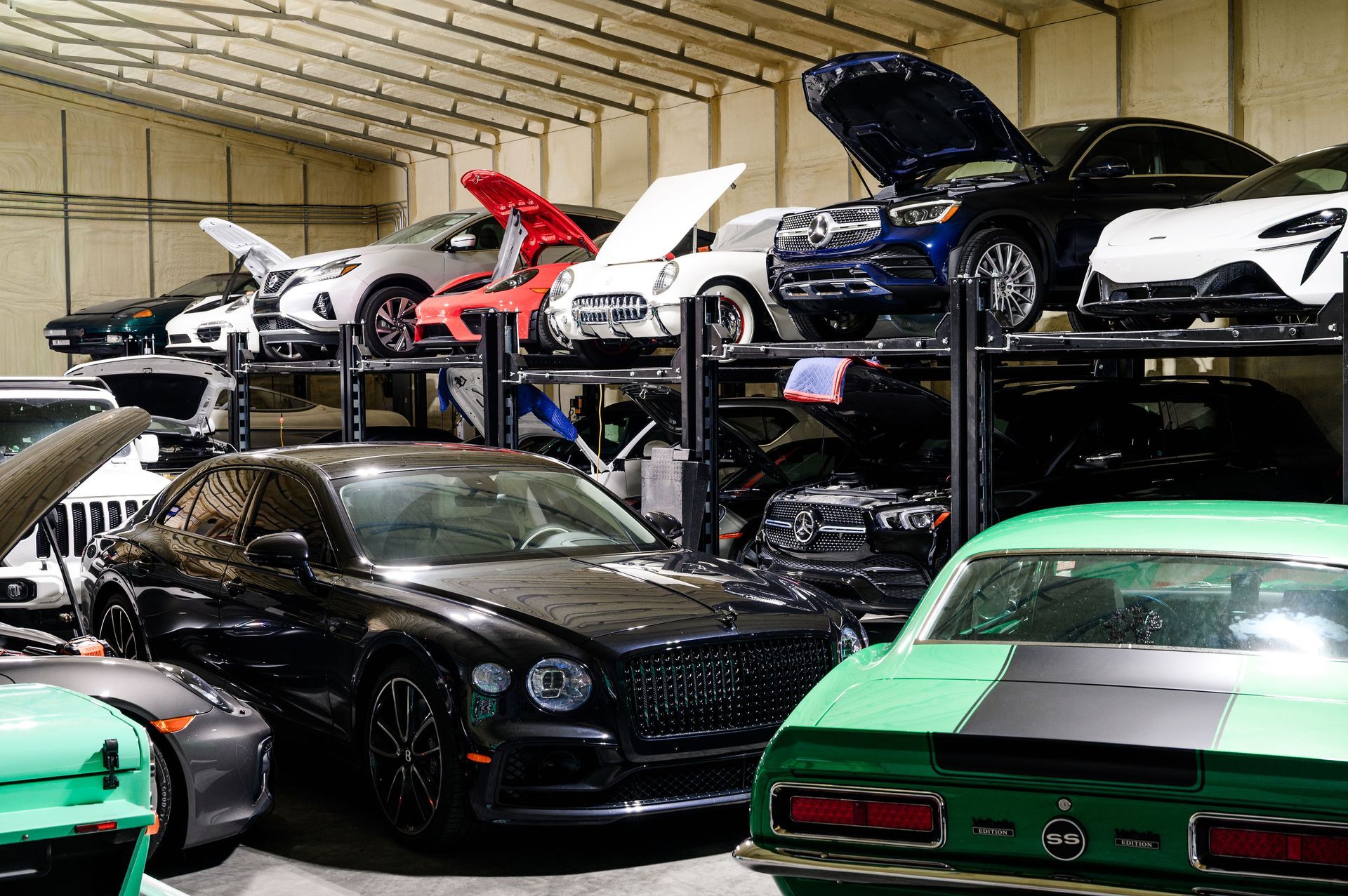 A collection of luxury and classic cars parked in a warehouse on multiple storage racks and the ground floor.