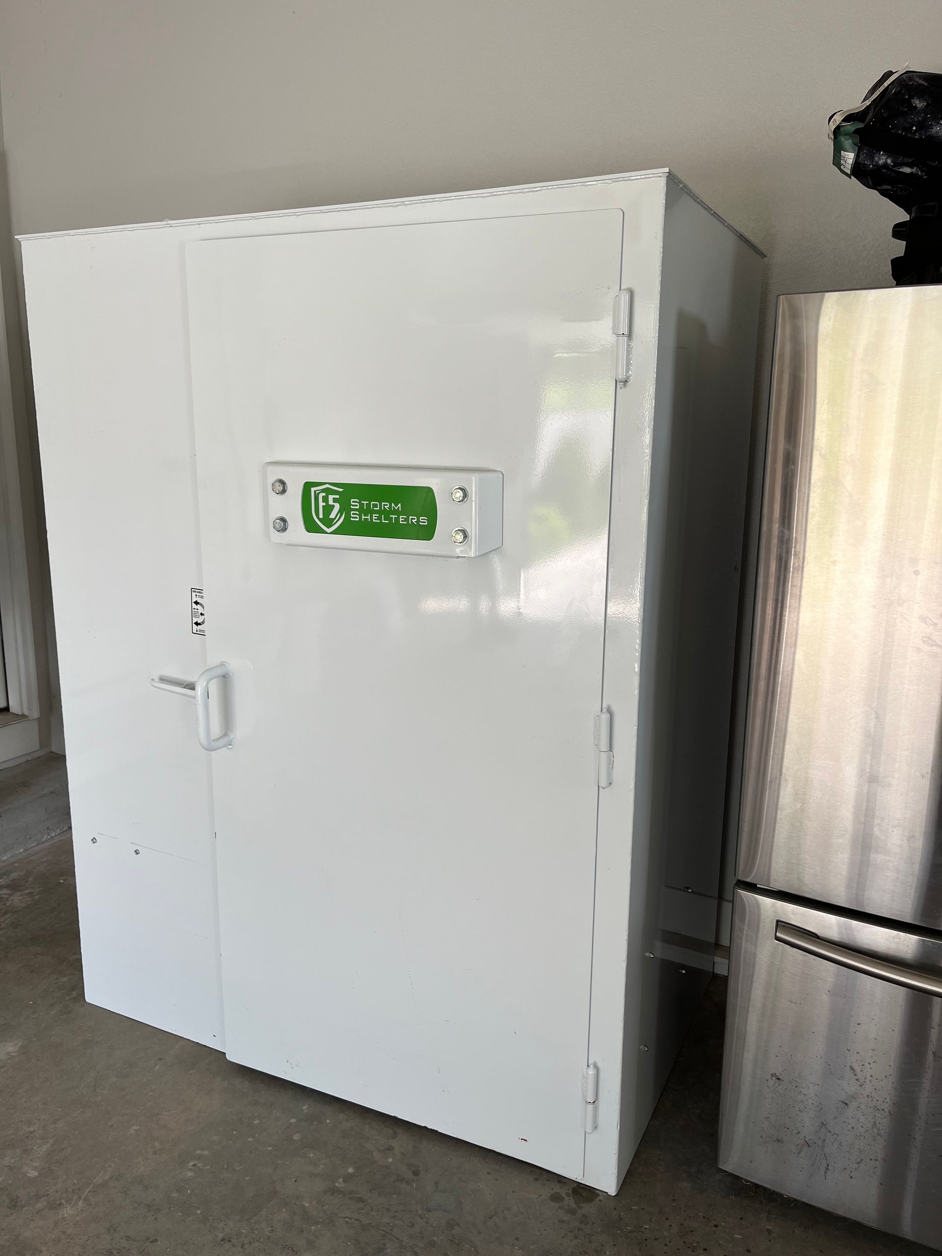 White industrial freezer with green digital display beside stainless steel fridge in a warehouse
