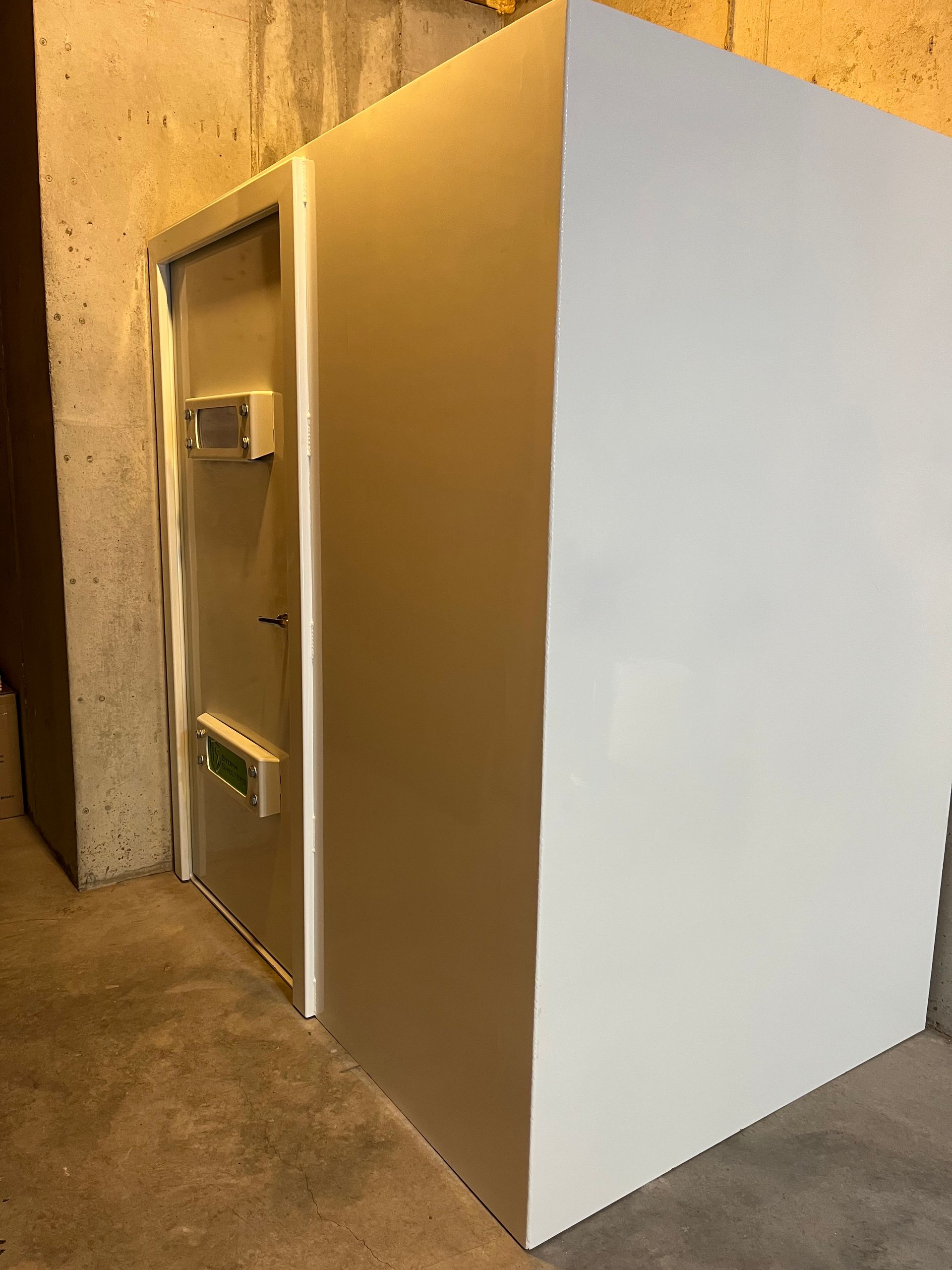 A white industrial machine or cabinet with a metal door in a narrow hallway or utility room.