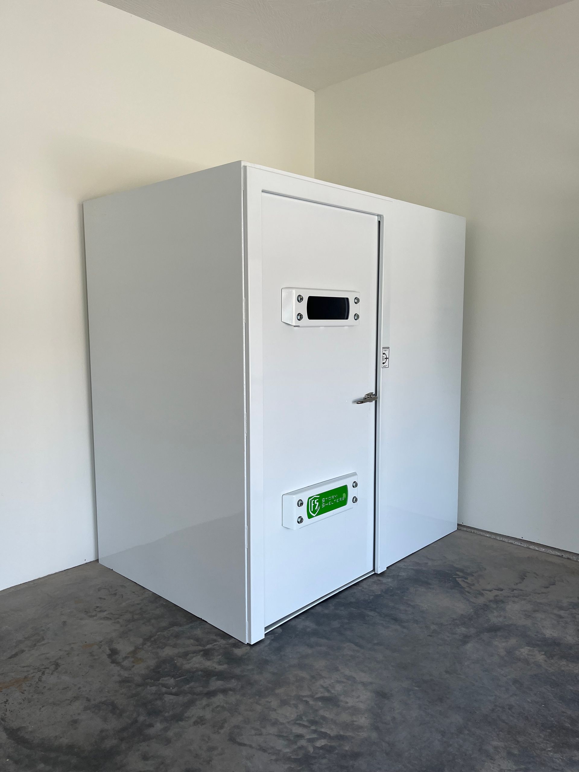 White insulated room with a door and small windows in a bare corner of a concrete-floored space