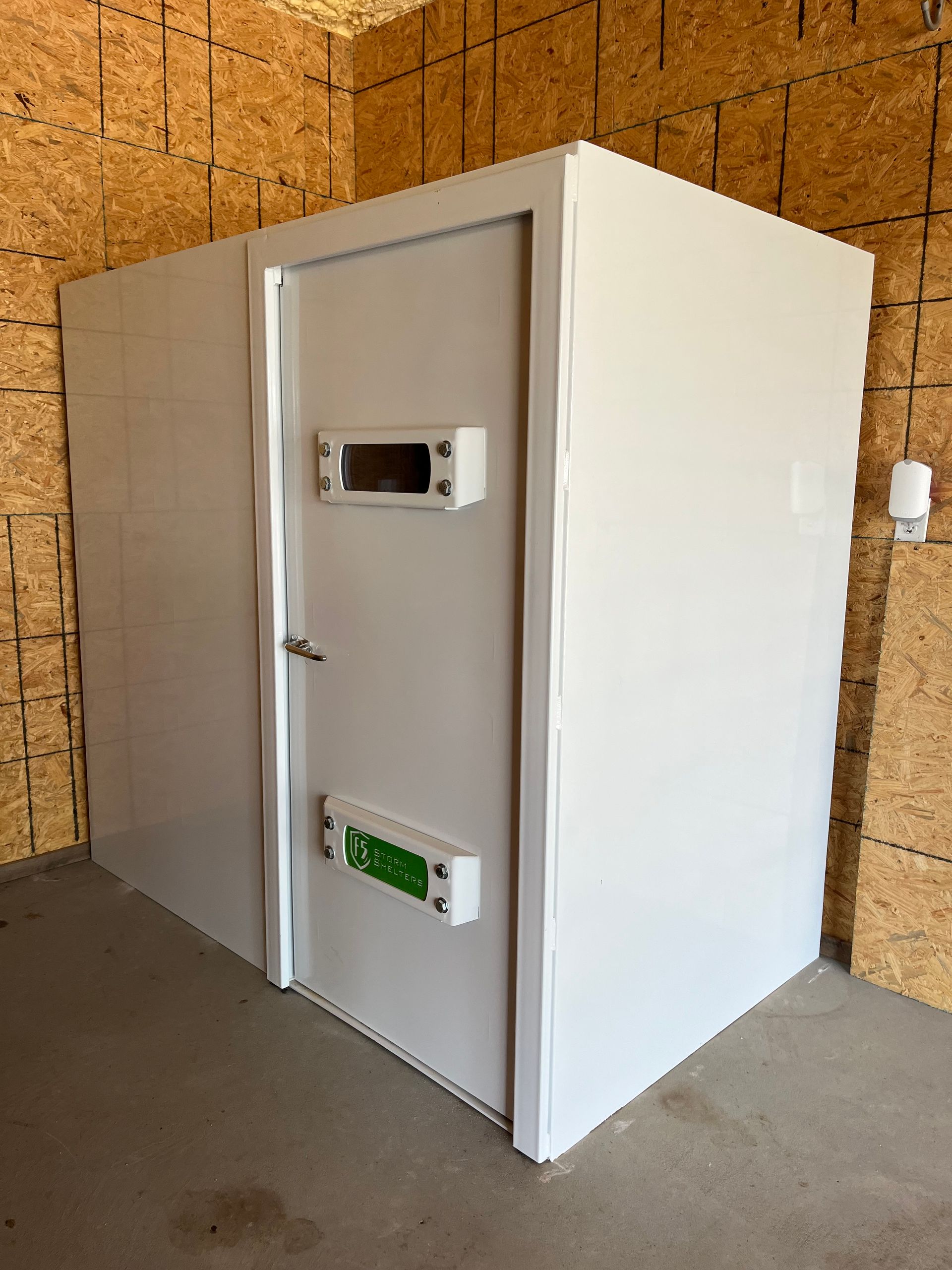 White walk-in cooler or freezer unit in a warehouse-like room with a closed door.