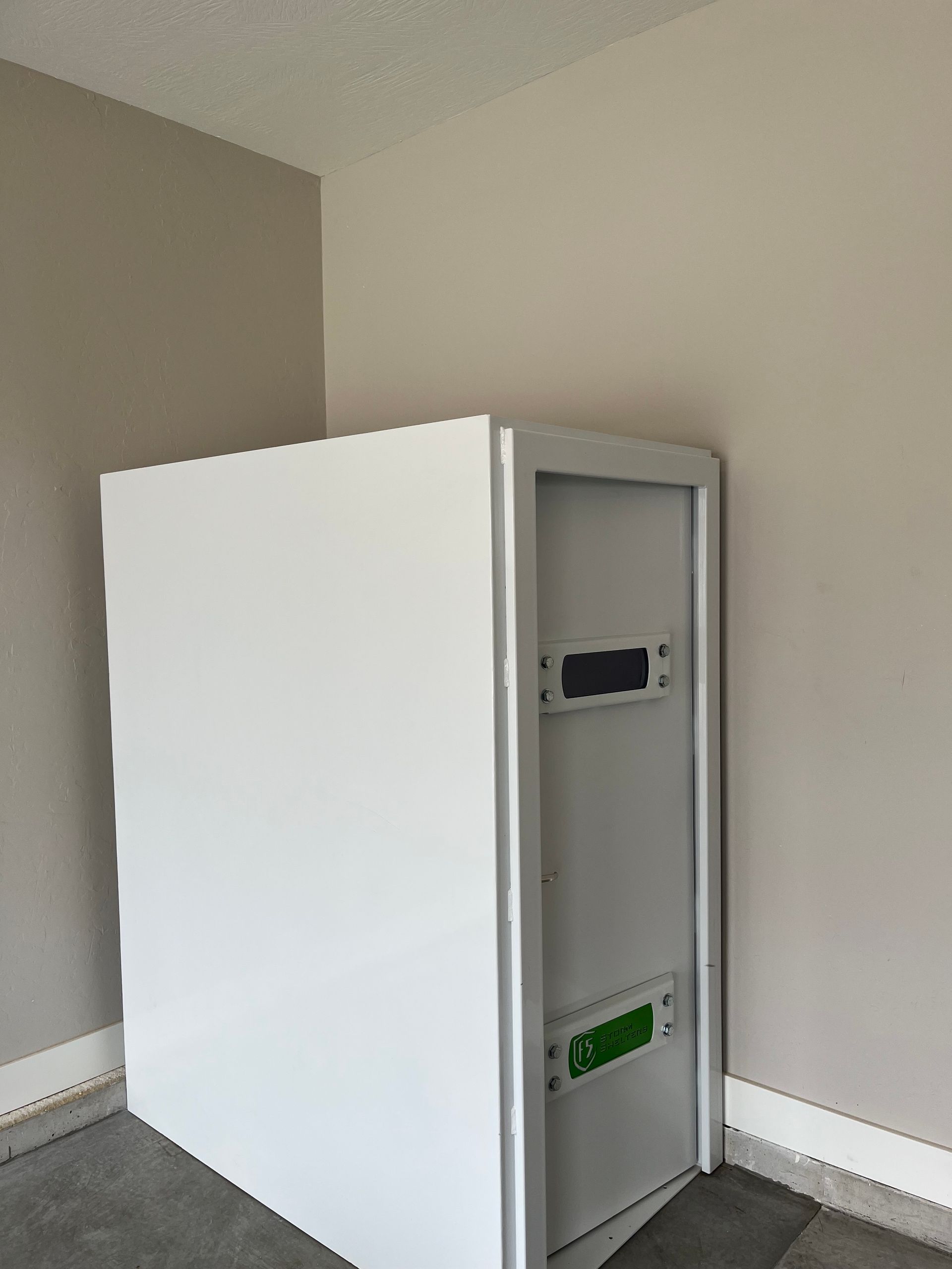 Small white metal cabinet or safe standing in a bare corner against beige walls and carpet.