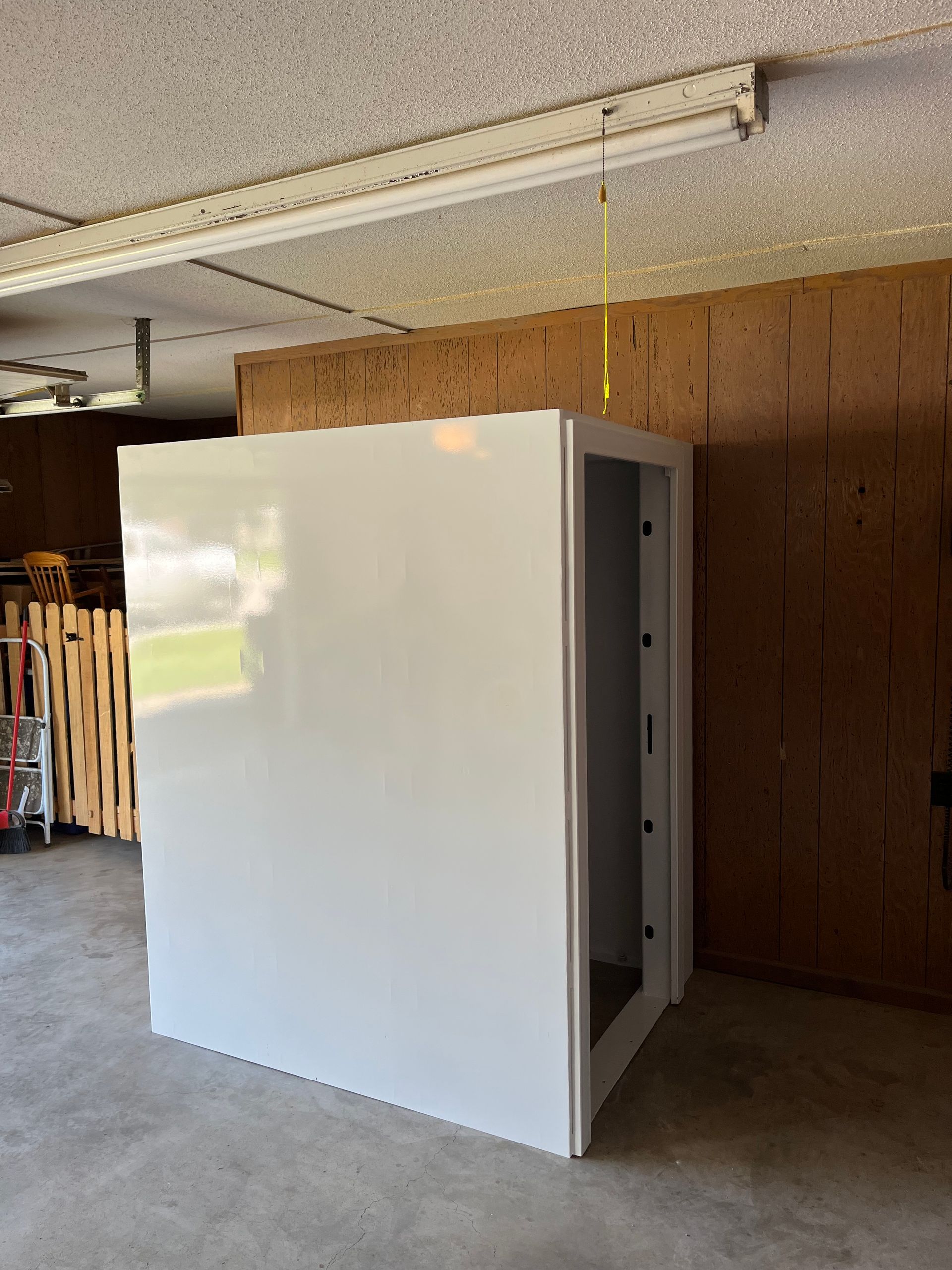 White walk-in storage cabinet in a garage, with open door and wood-paneled wall behind it