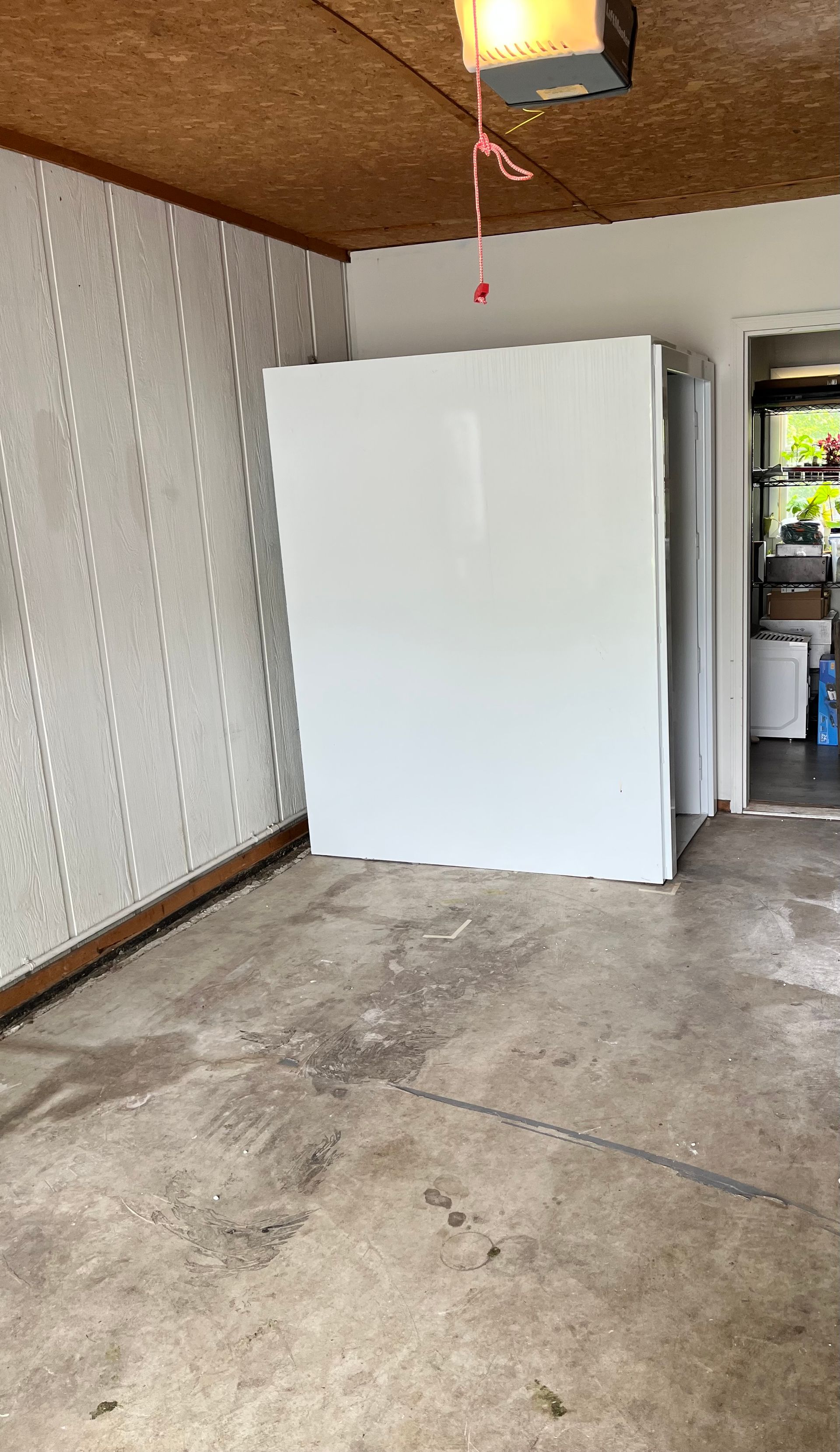 White freezer in a concrete garage with open doorway and hanging light fixture