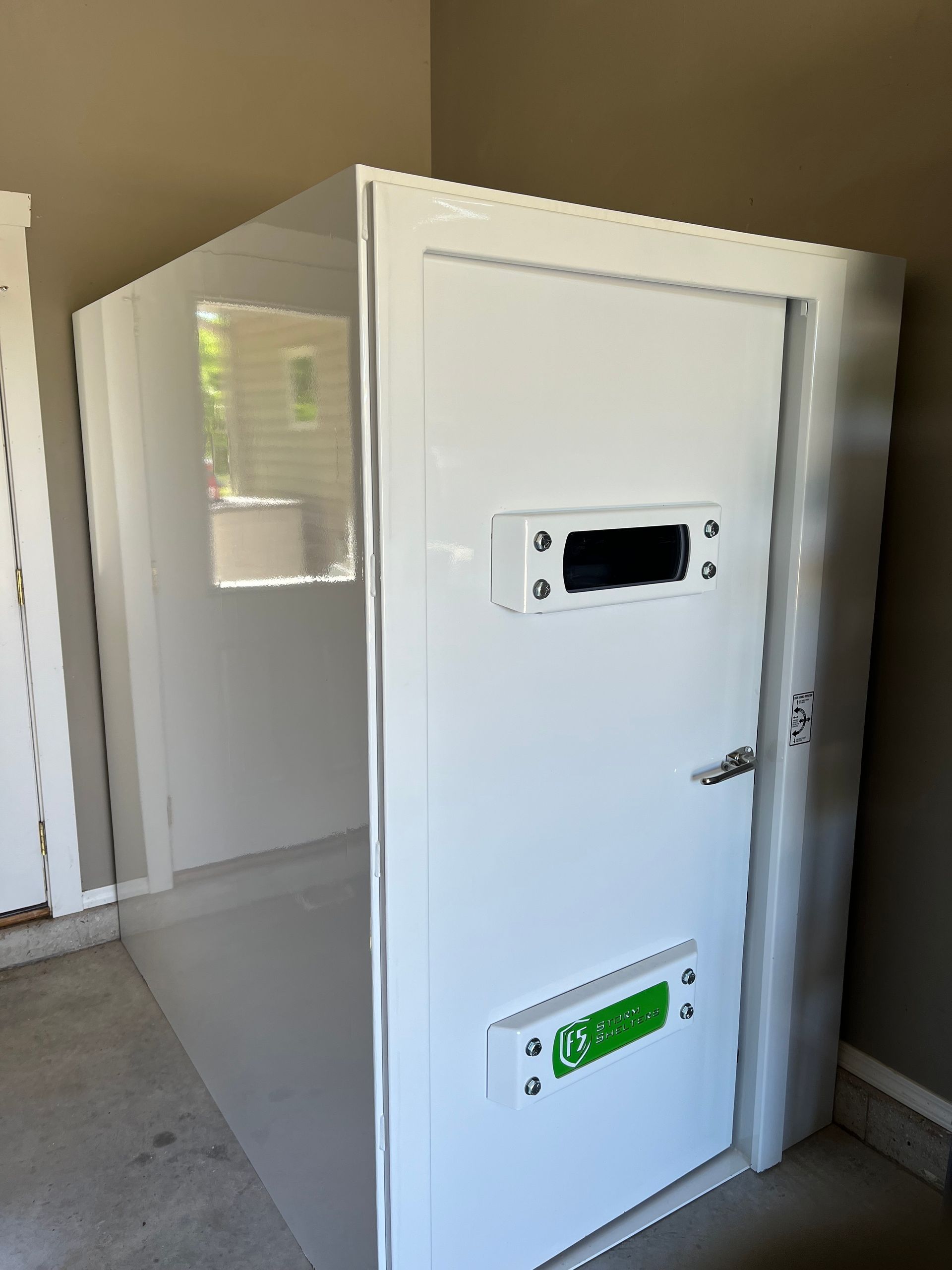 White utility room with an open door and wall-mounted panels, viewed from a concrete hallway.