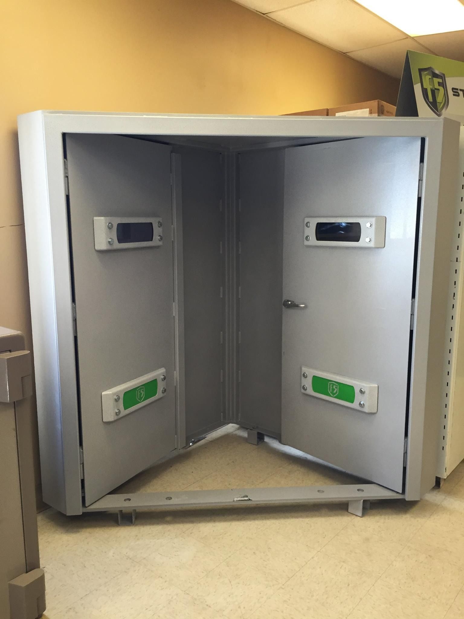 Open cabinet with two gray doors and wall-mounted control panels inside, in a room.