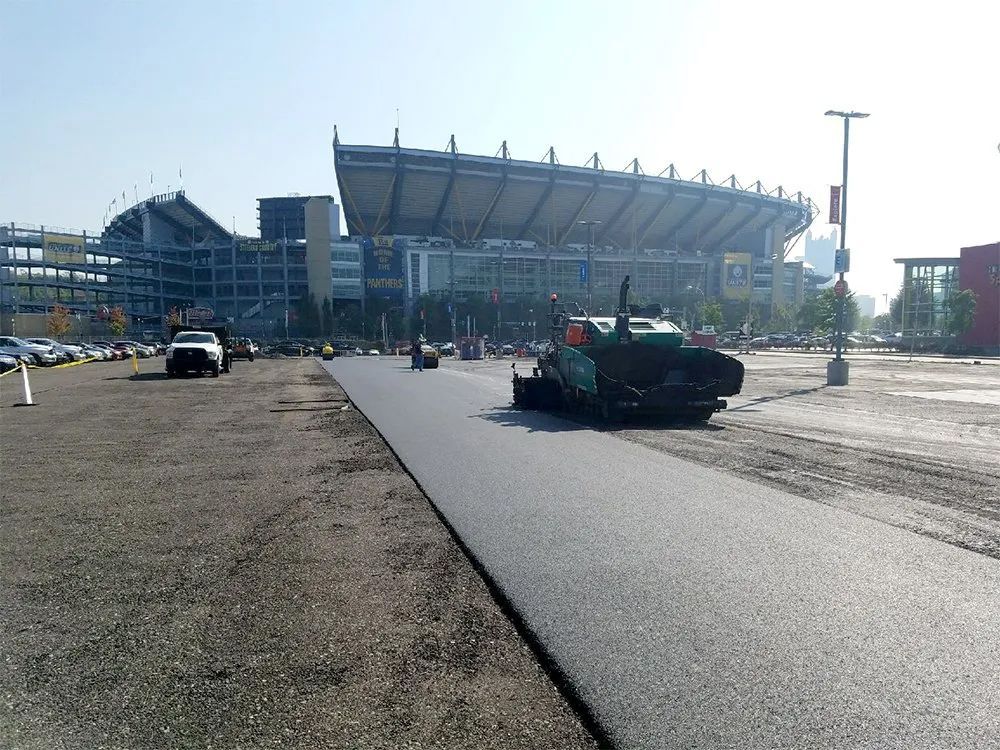 A road is being paved in front of a large stadium