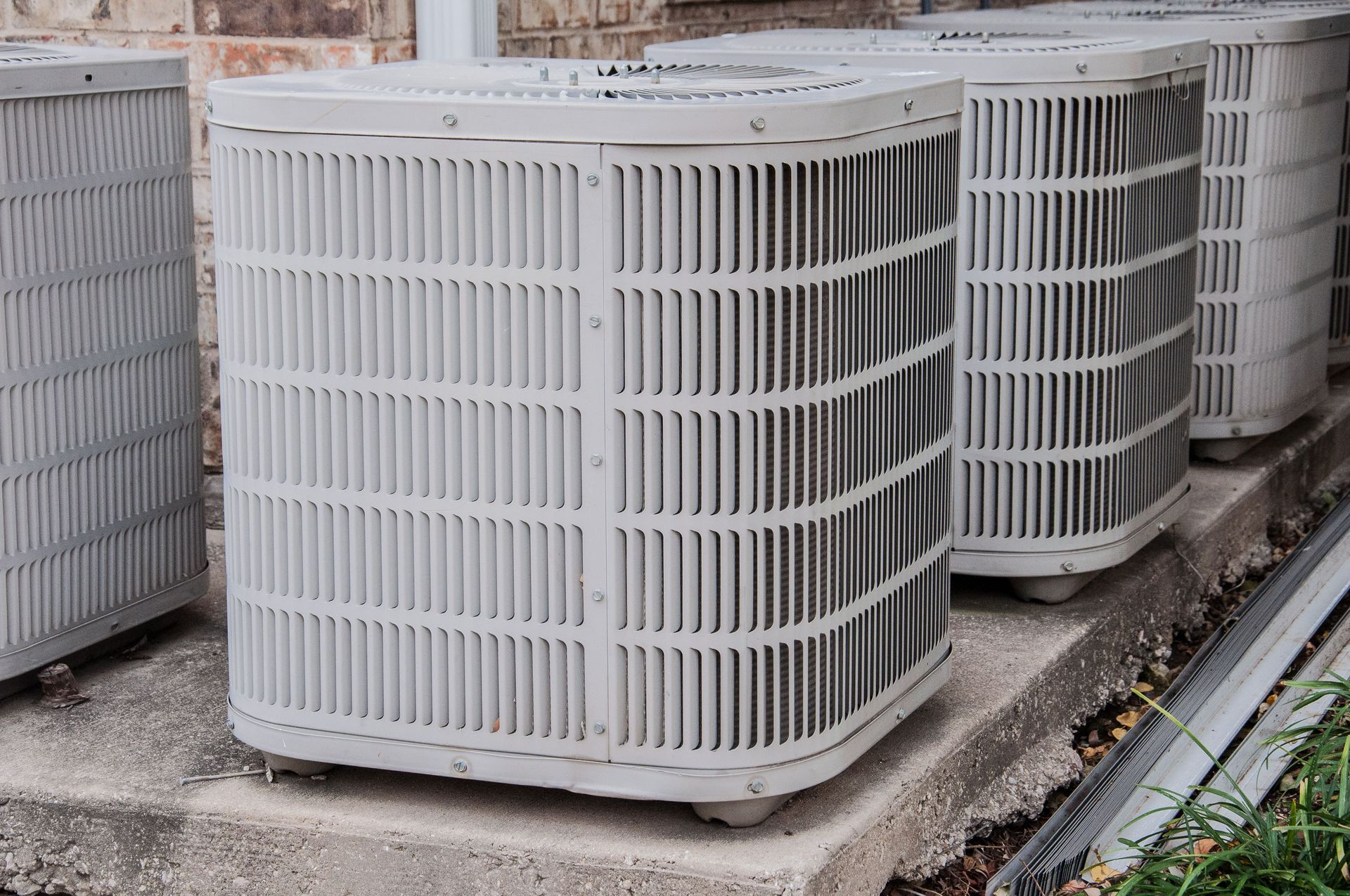 Stacked white outdoor air-conditioning units lined up beside a building.