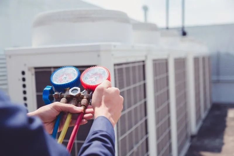 Technician checking HVAC refrigerant gauges on rooftop air conditioning units