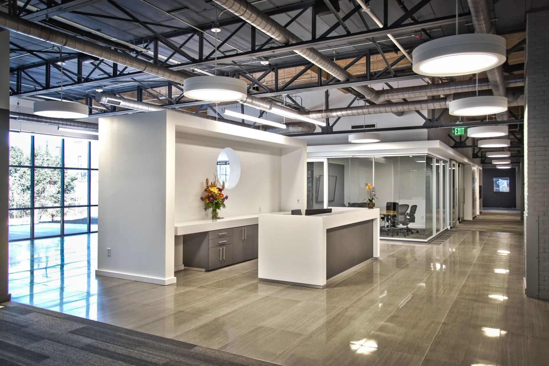 Modern office lobby with polished floors, white reception desk, exposed beams, and large windows