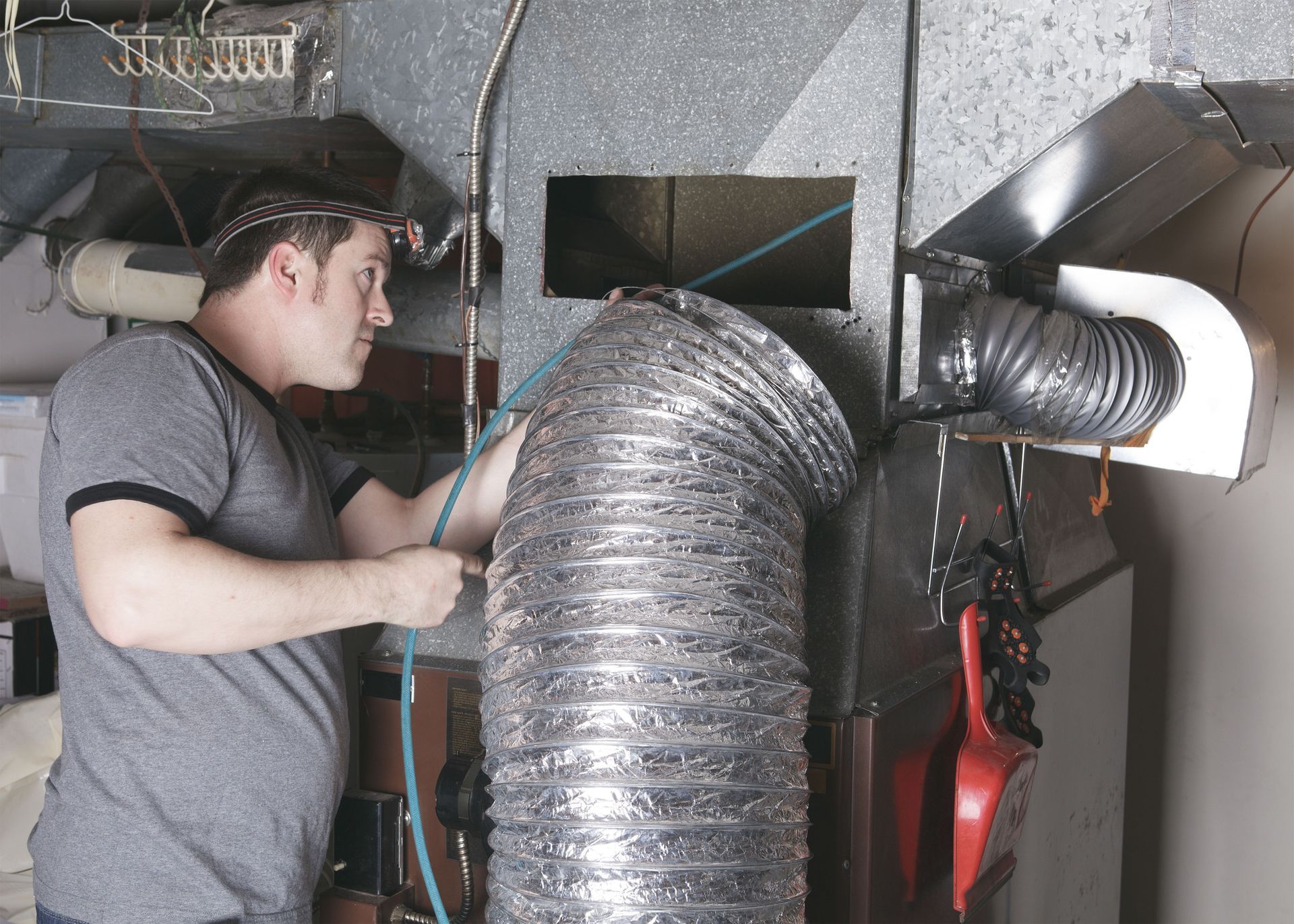 Worker inspecting large silver ventilation duct in a utility room