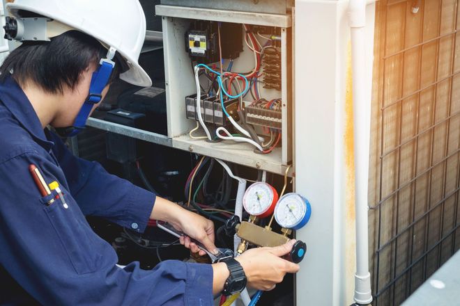 Technician inspecting HVAC unit with gauges and tools beside an outdoor electrical panel
