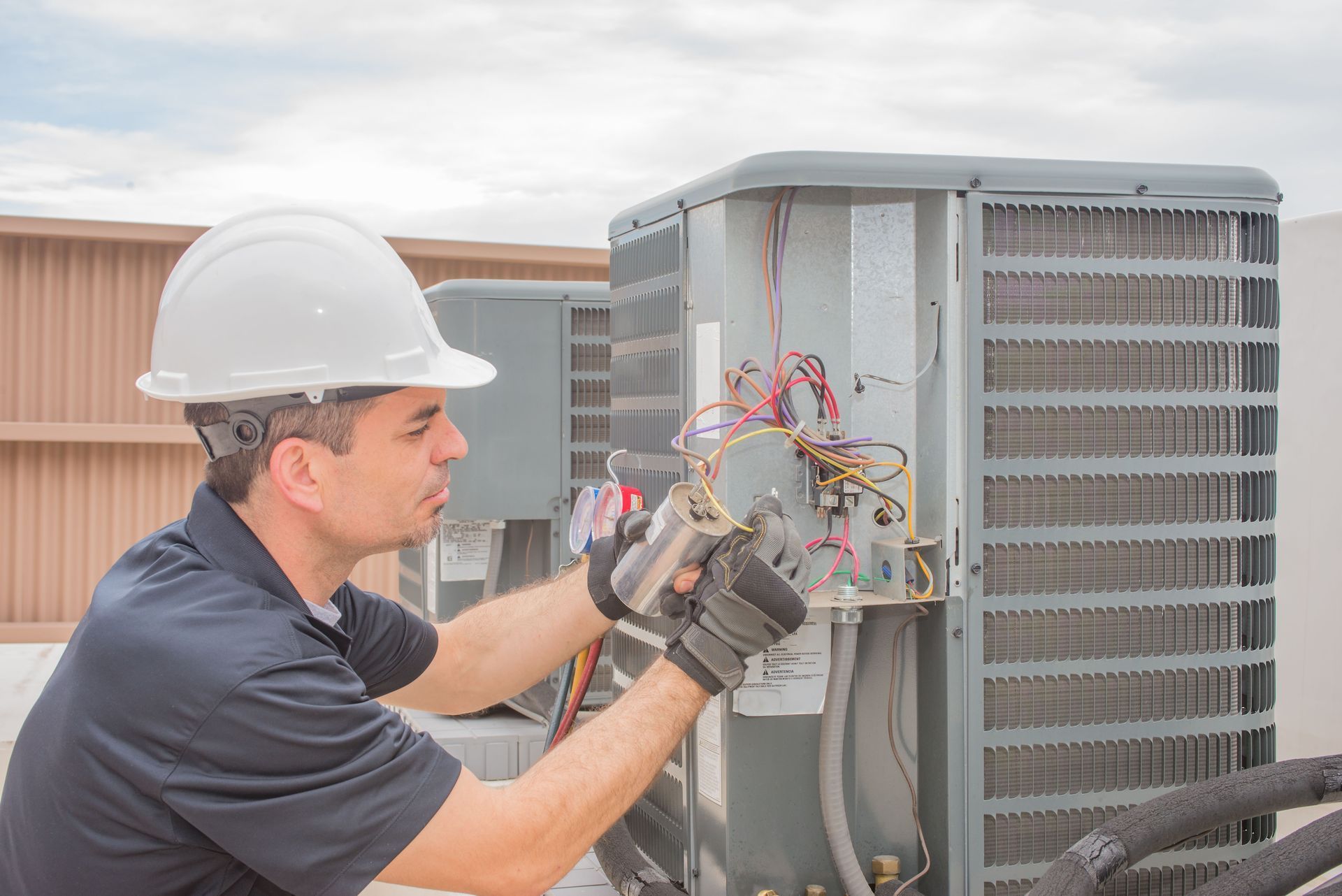 Technician in hard hat inspecting HVAC unit wiring outdoors