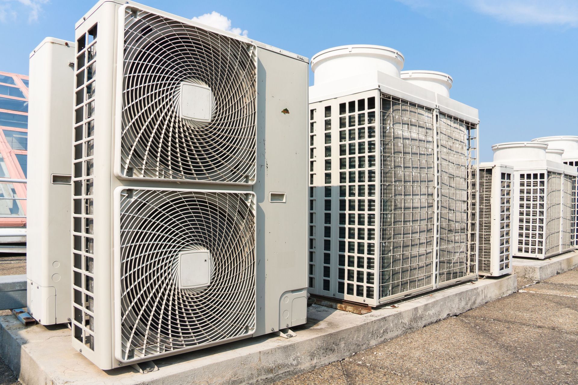 Row of rooftop HVAC units with large metal fans and vents under a clear sky