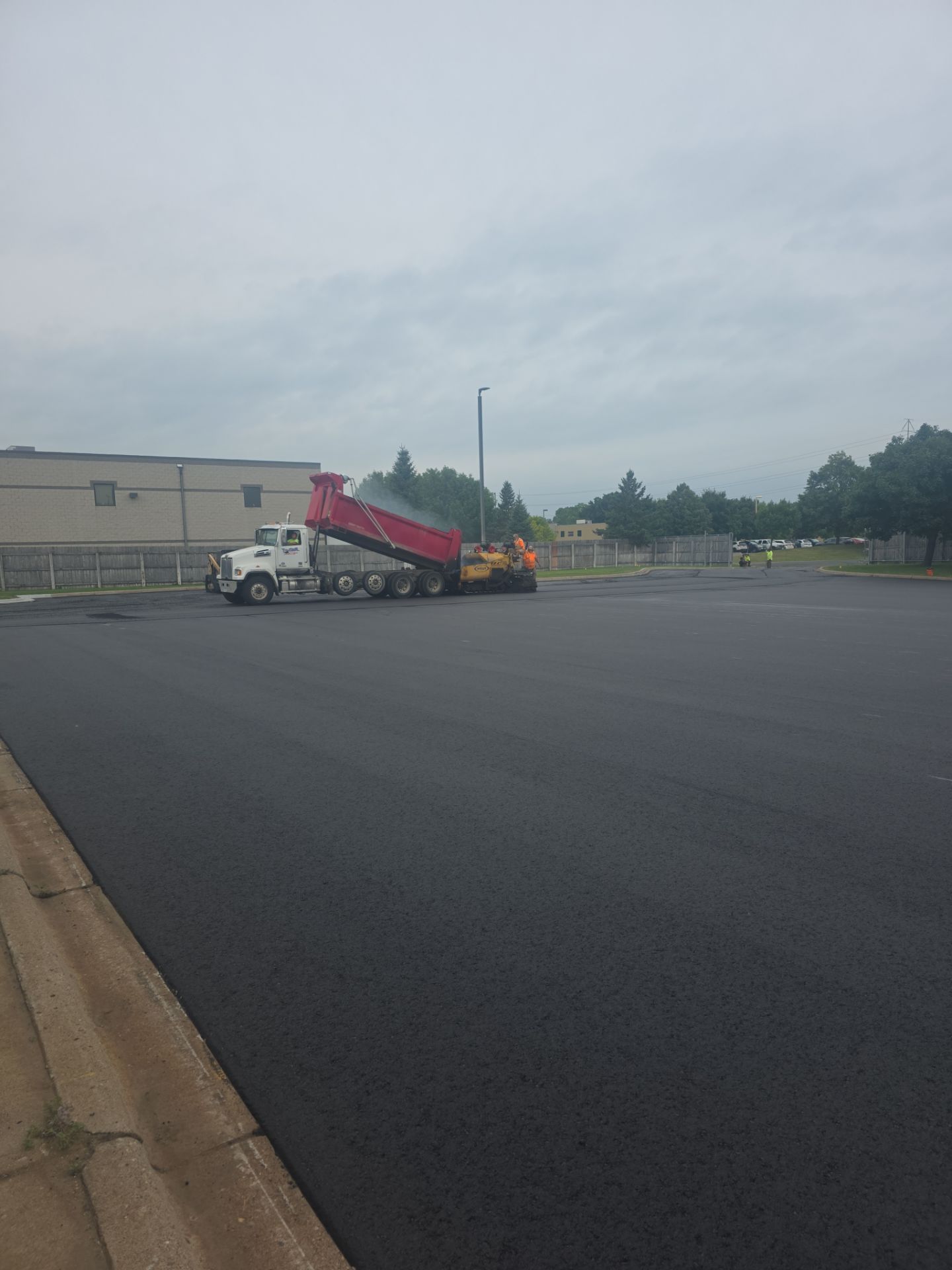 Tow truck hauling a red dump truck in a parking lot under an overcast sky