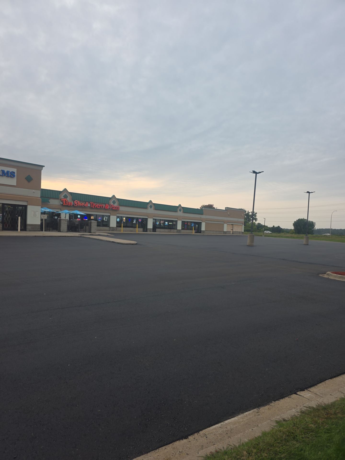 Empty shopping center parking lot at dusk with storefronts and cloudy sky