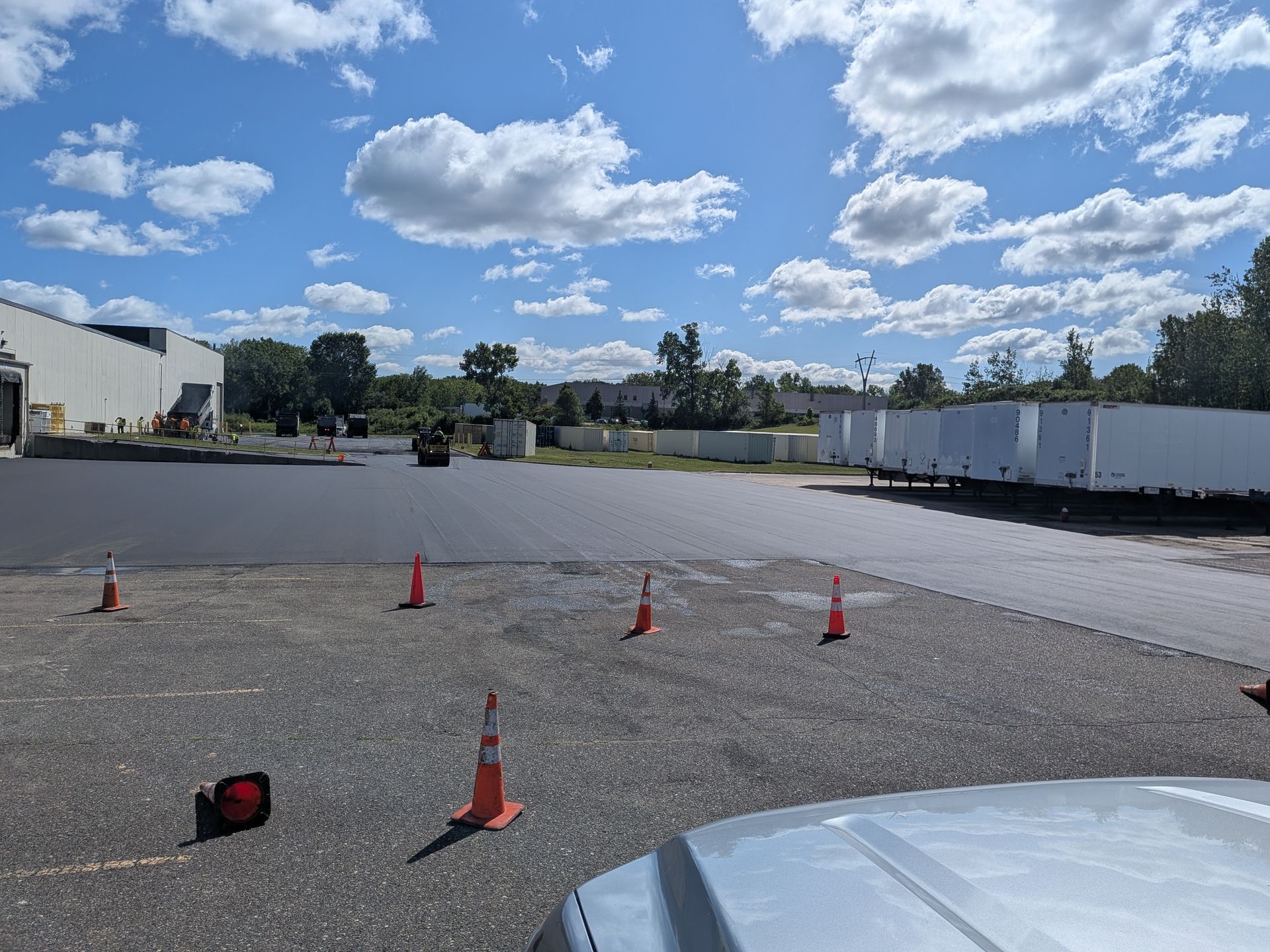 Empty parking lot with orange cones under a cloudy blue sky, trailers in the background